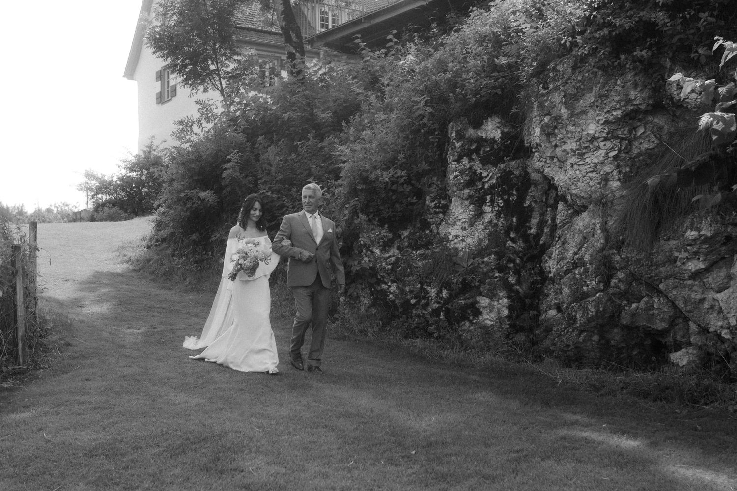 Black and white photo of couple walking along garden path beside stone wall.