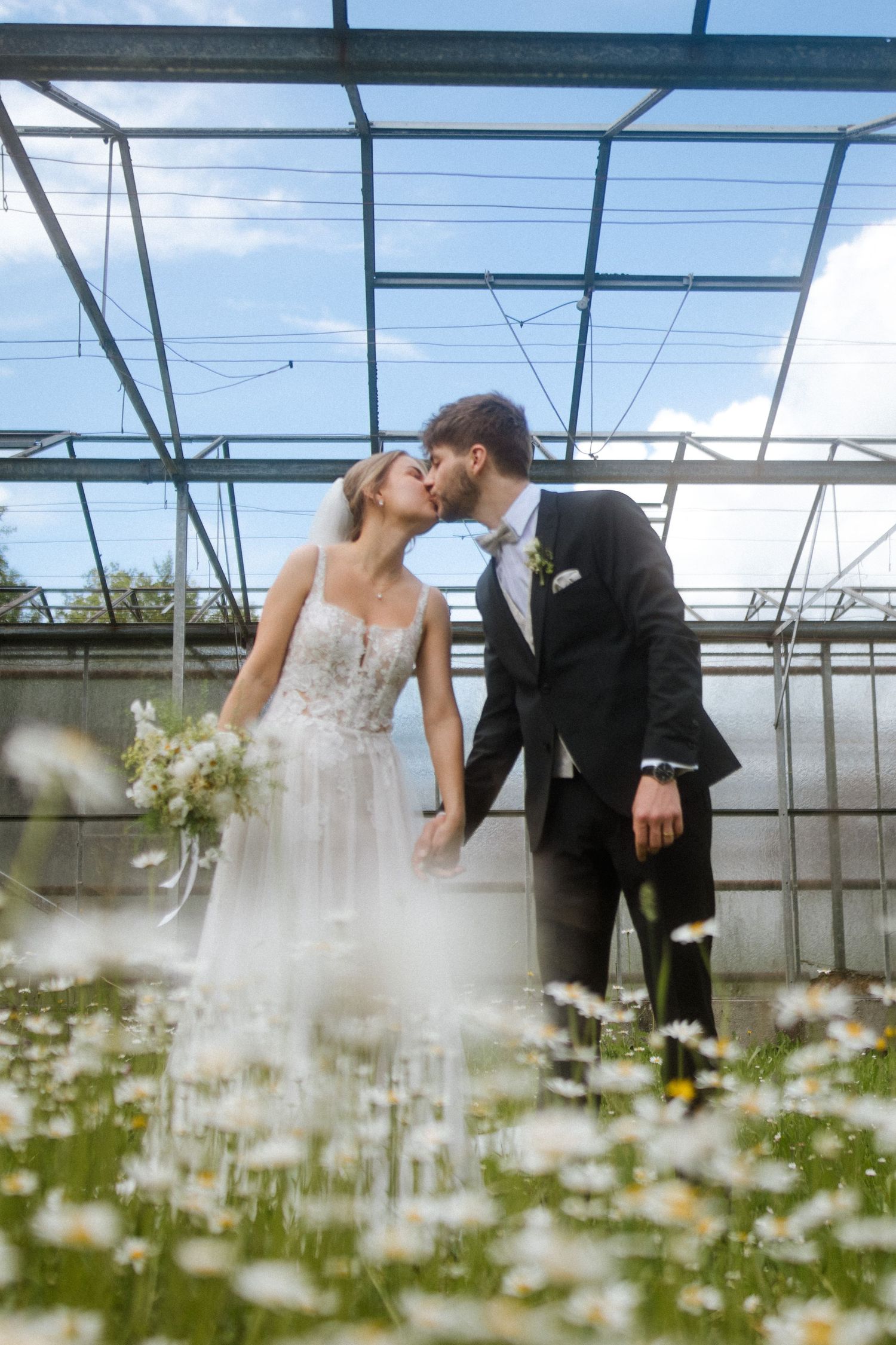 Wedding couple shares an intimate moment in a greenhouse filled with blooming daisies.