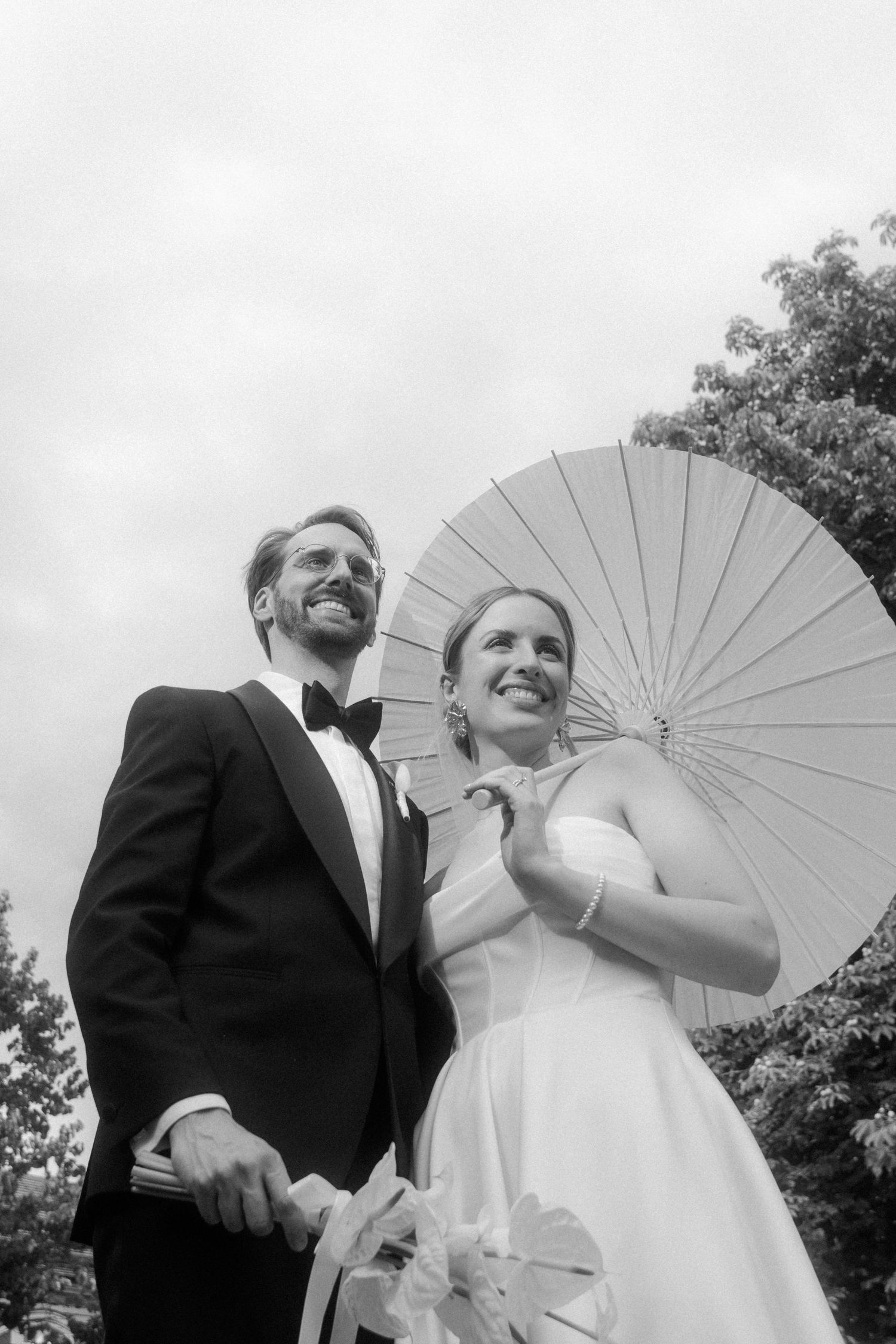 Wedding couple shares joyful moments under a white parasol outdoors.
