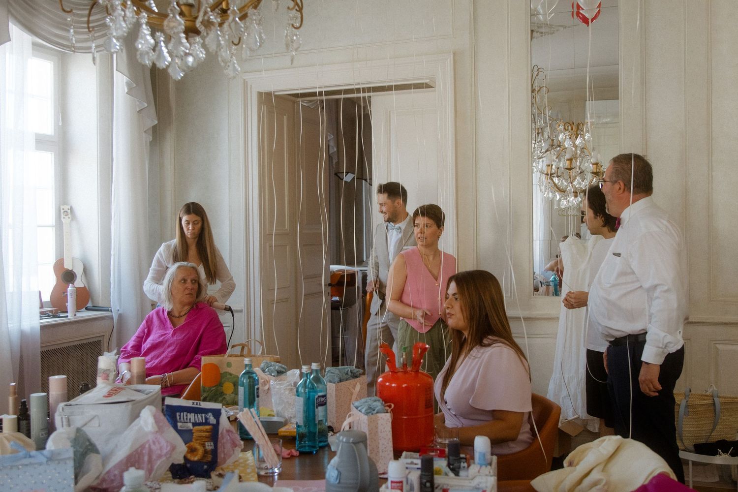 Bright room with people preparing for a special event, featuring elegant decor and natural lighting.