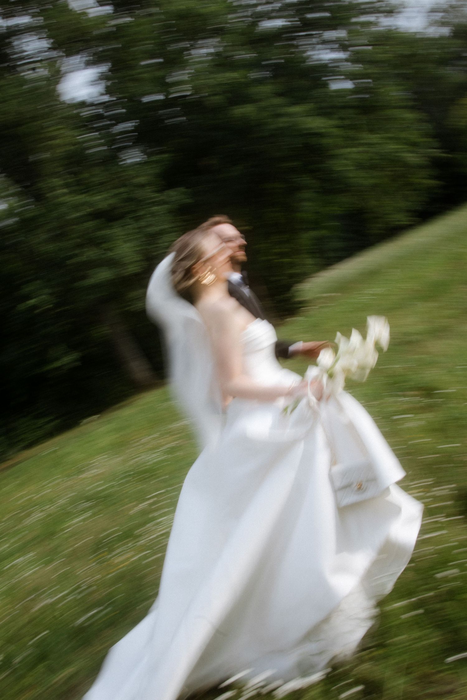 Motion-blurred photo of a bride twirling in a white dress outdoors.