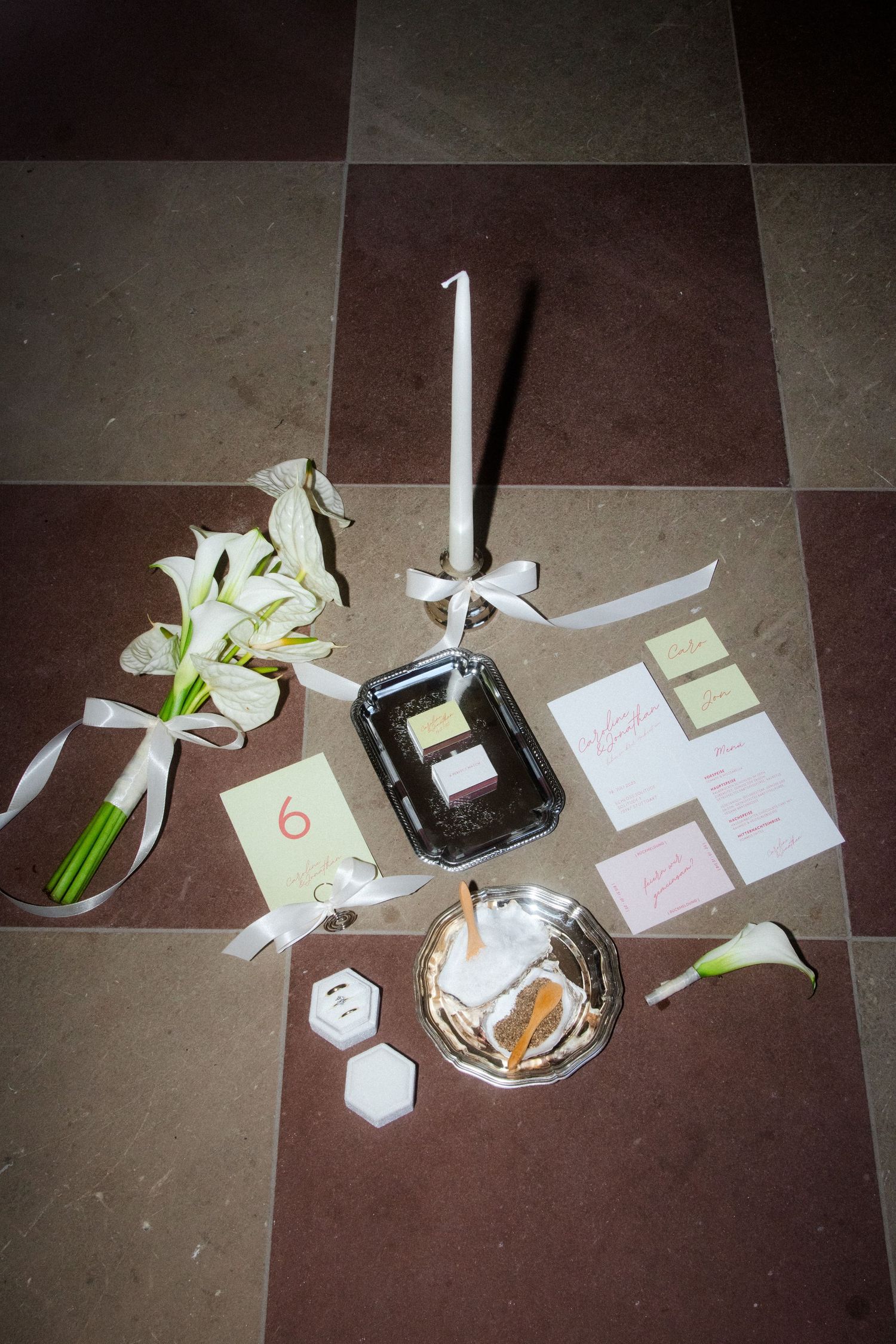 Wedding invitation suite with cards, envelopes and decorative elements arranged on dark floor tiles.
