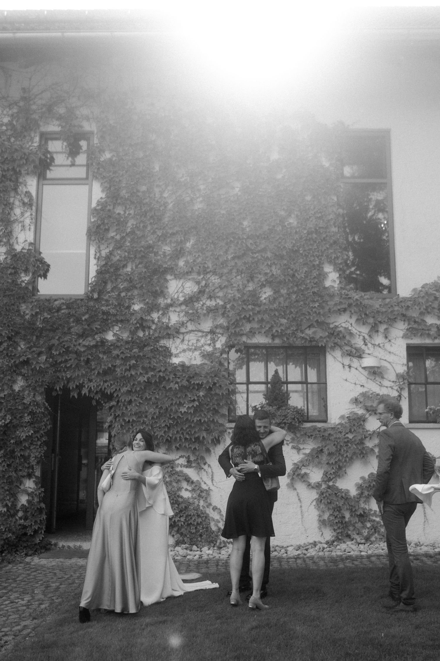 Black and white image of wedding guests gathered outside historic ivy-covered building.
