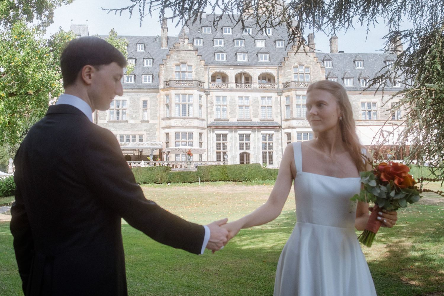 Wedding couple walking on manicured lawn with grand historic estate building in background.