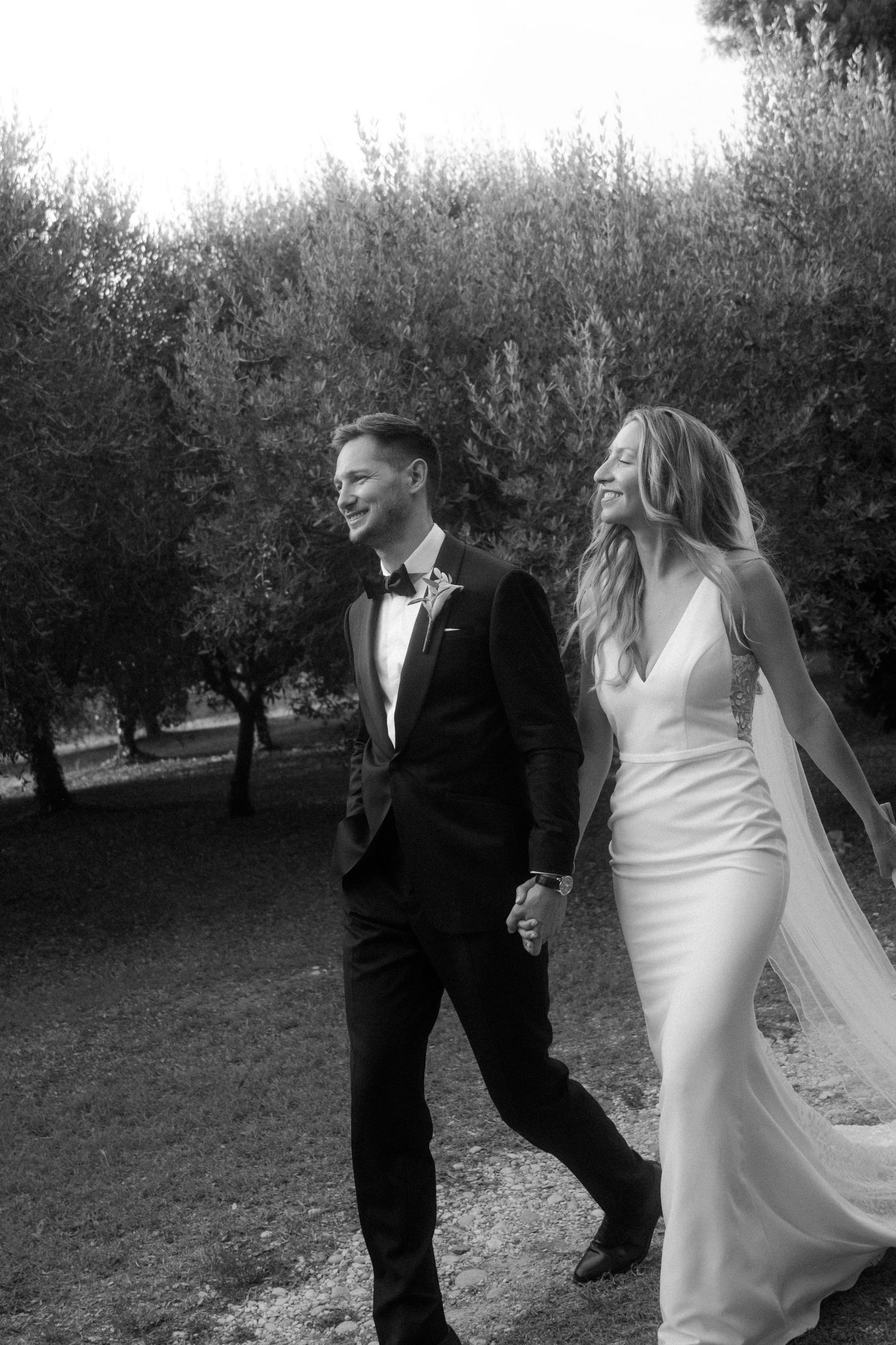 Black and white wedding photos showing a couple walking through an olive grove.