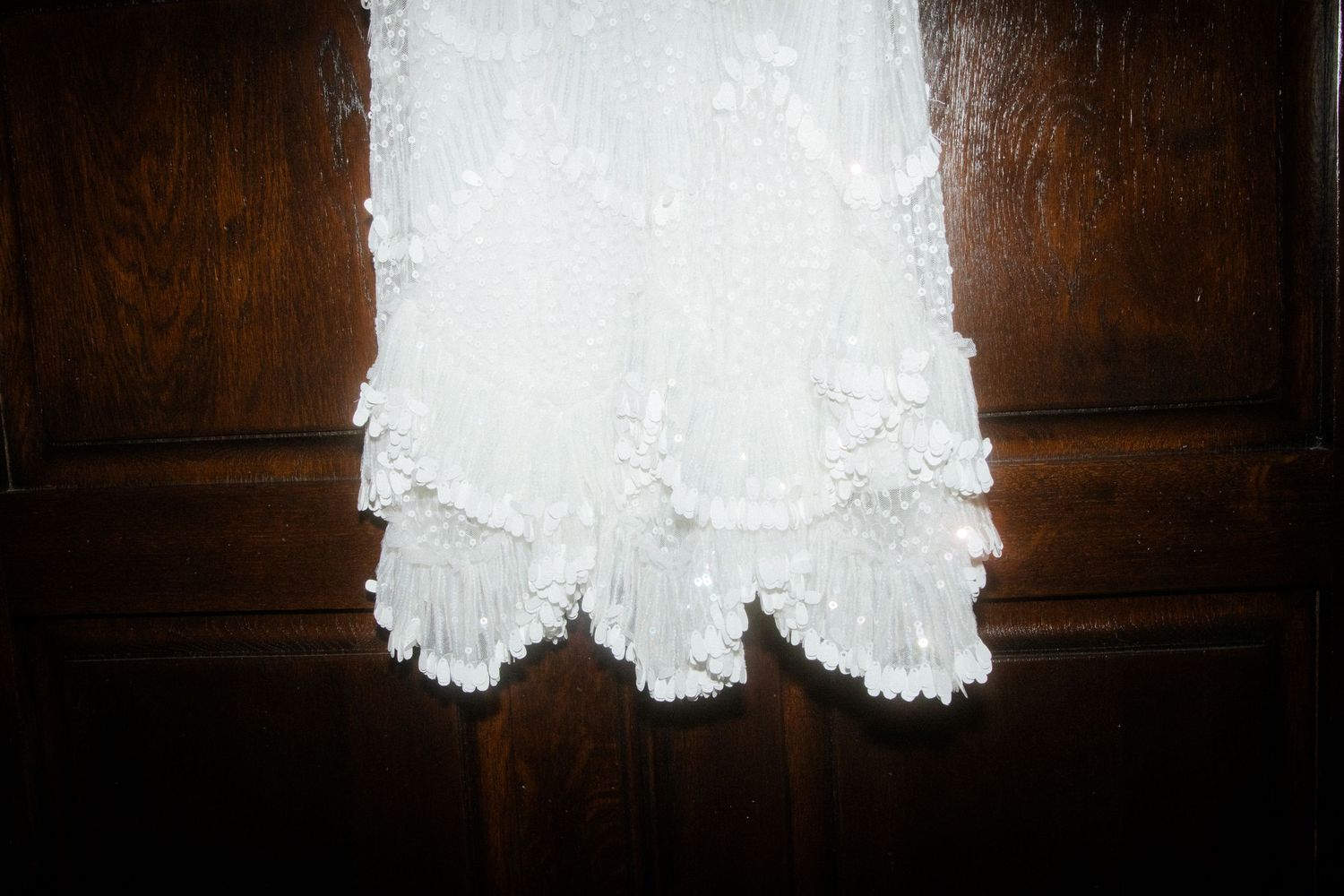 Close-up of white lace detail on a wedding dress hem against dark wood.