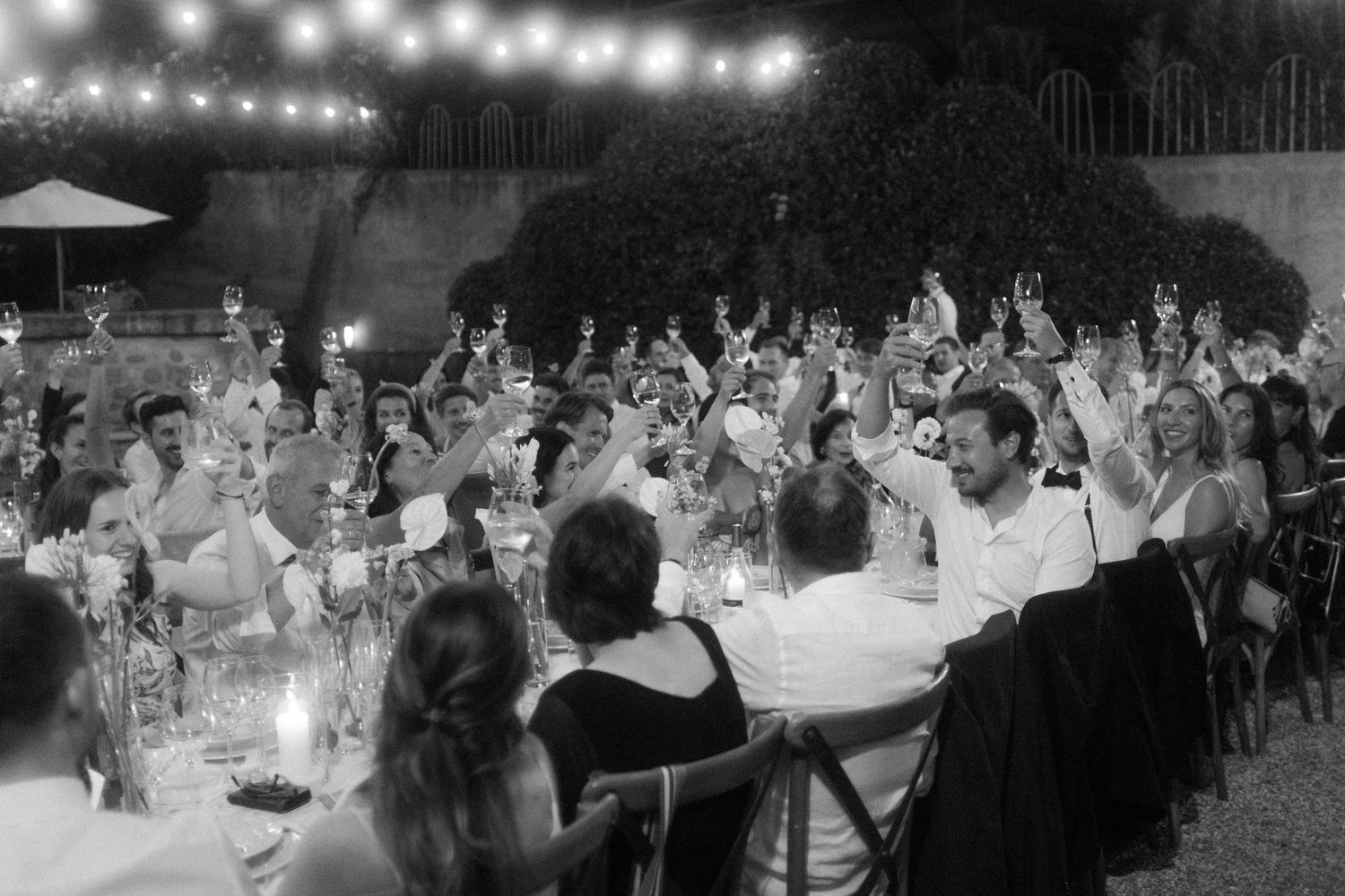 Wedding reception guests dance and celebrate under string lights at an outdoor evening party.