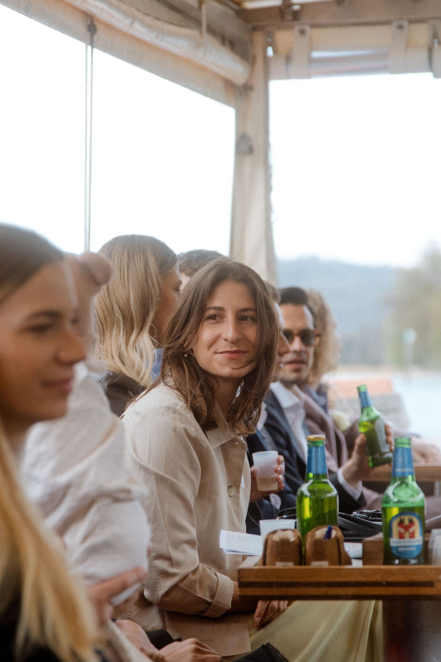 Wedding guest smiling on boat with drinks on wooden table during reception.