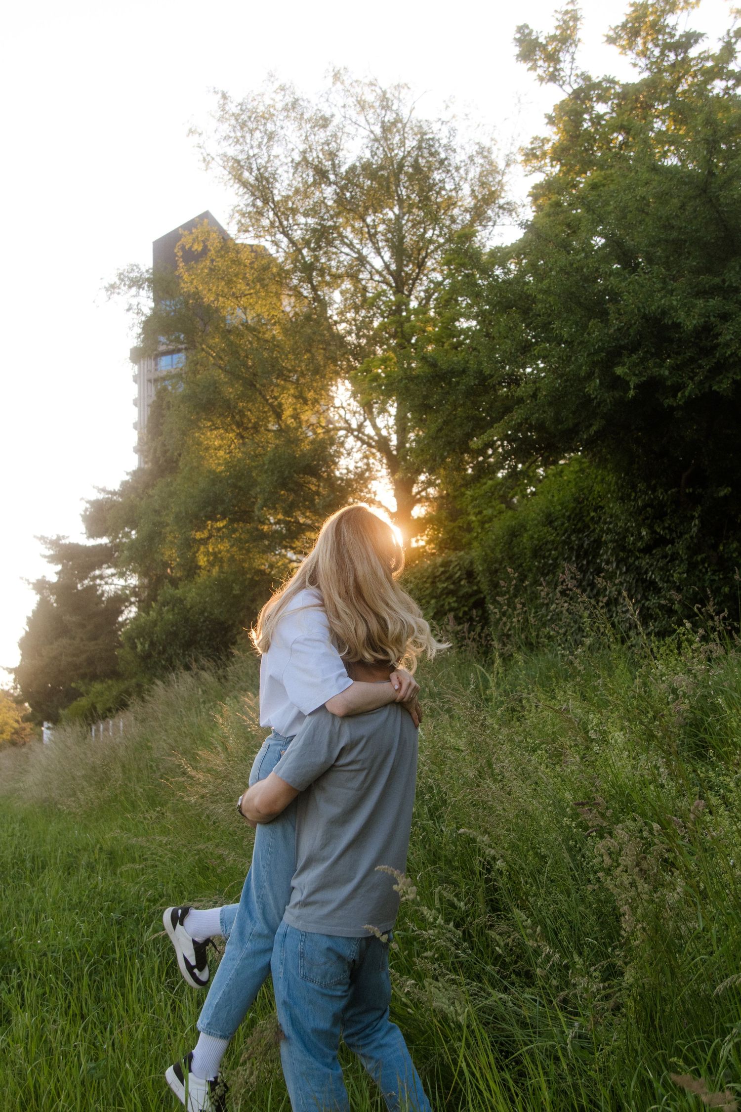 A couple walks hand in hand through tall grass and trees during golden hour.