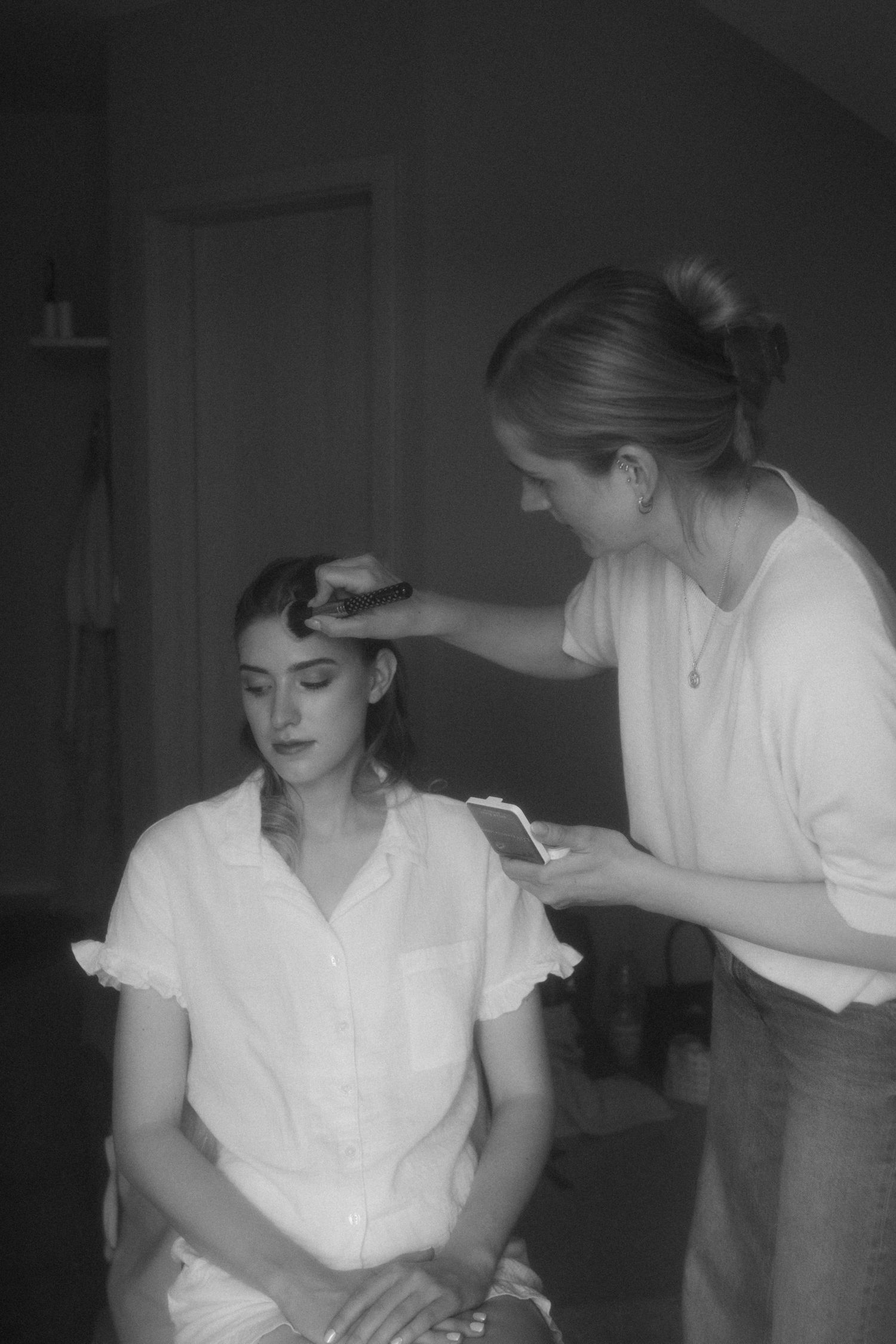 A black and white photo of a stylist working on someone's hair during wedding preparations.