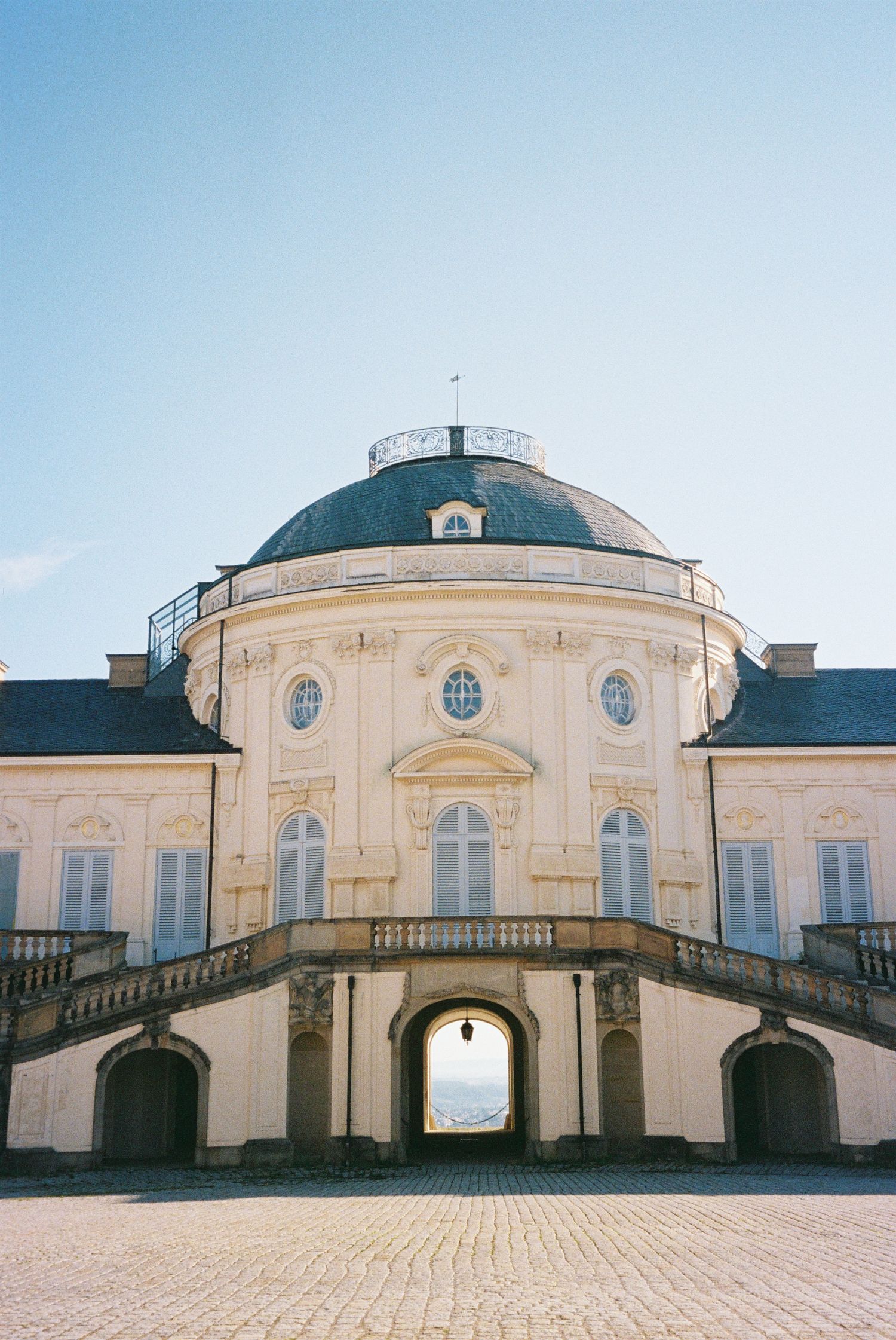 Panoramic view of a classical European palace building with domed roof and symmetrical architecture against blue sky.