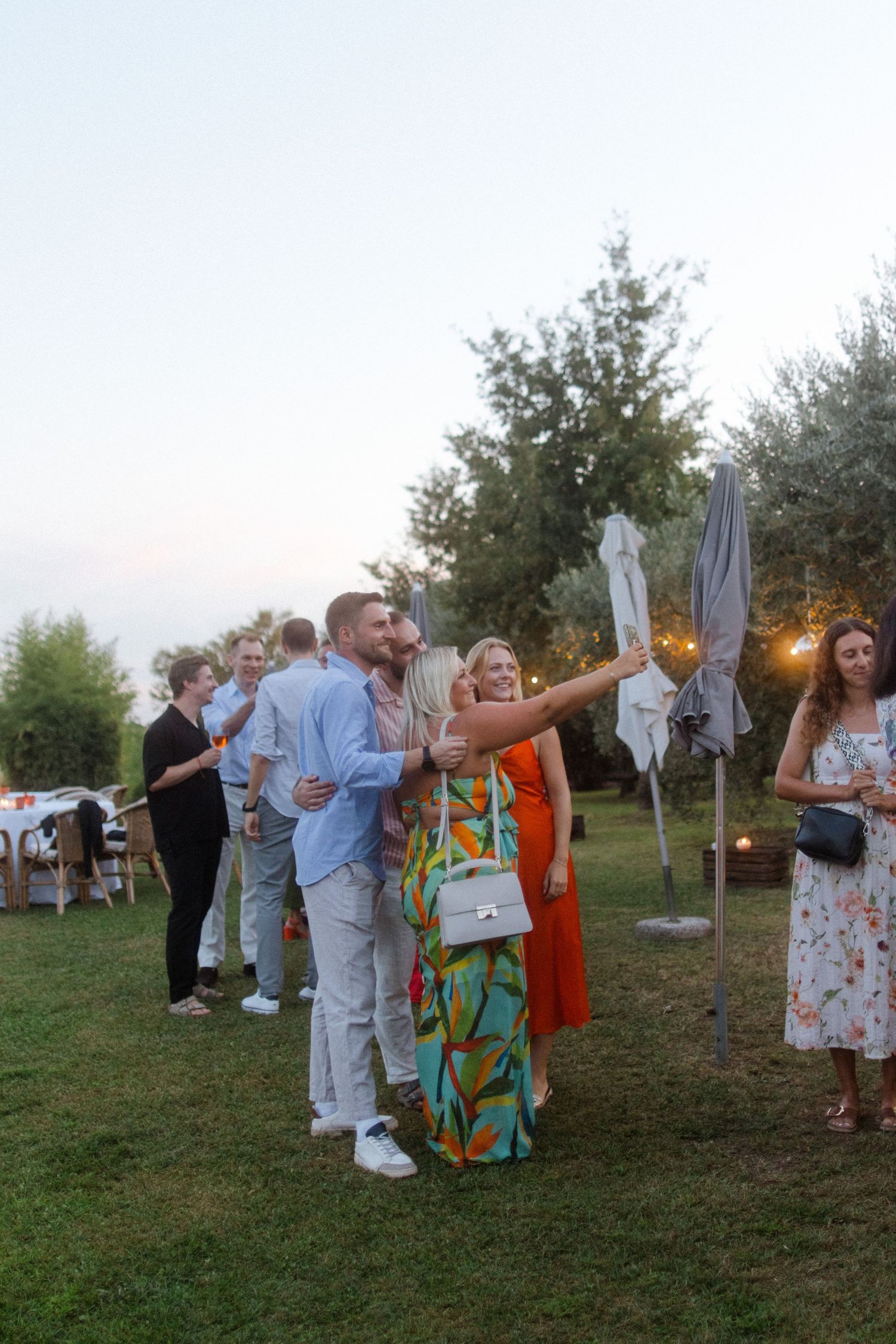 Party guests dancing and celebrating on a grassy lawn during sunset.
