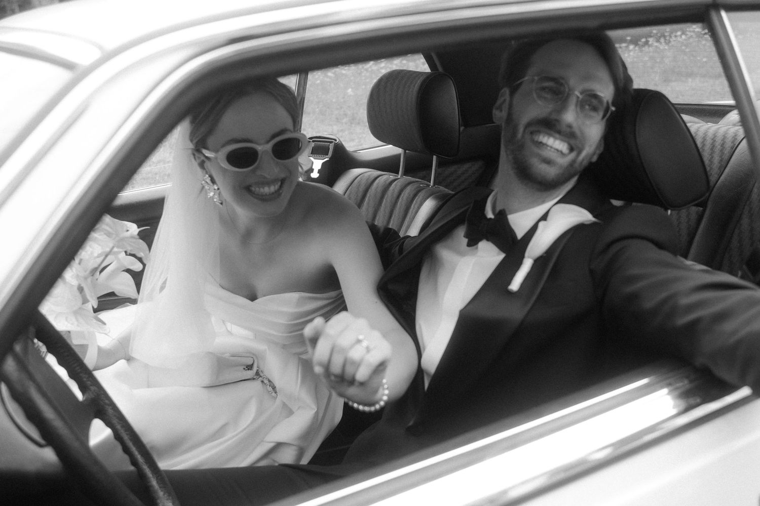 A couple shares a joyful moment inside a car on their wedding day.
