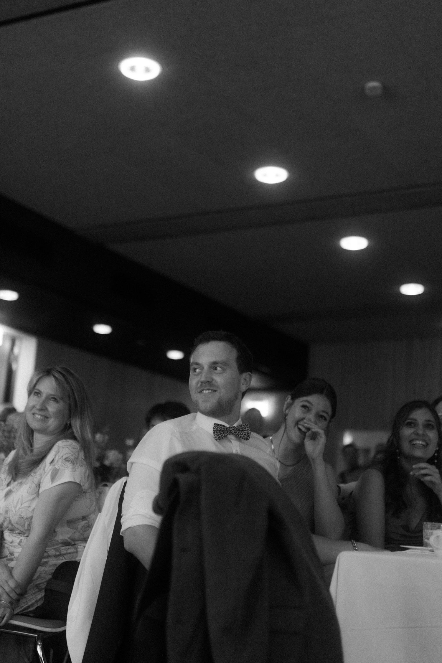 Black and white photo of reception guests enjoying entertainment from their seats.