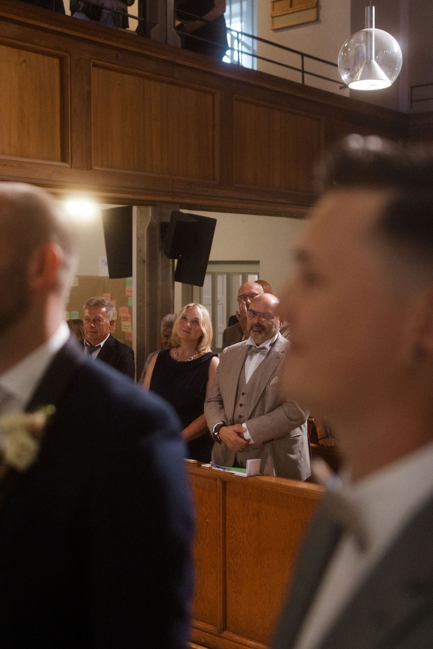 Wedding guests observe ceremony from wooden church pews.