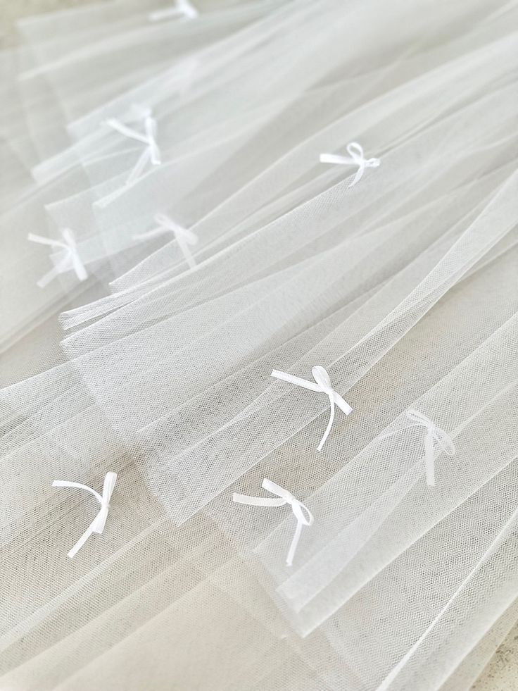 Delicate white tulle fabric with small bow details in a repeating pattern.