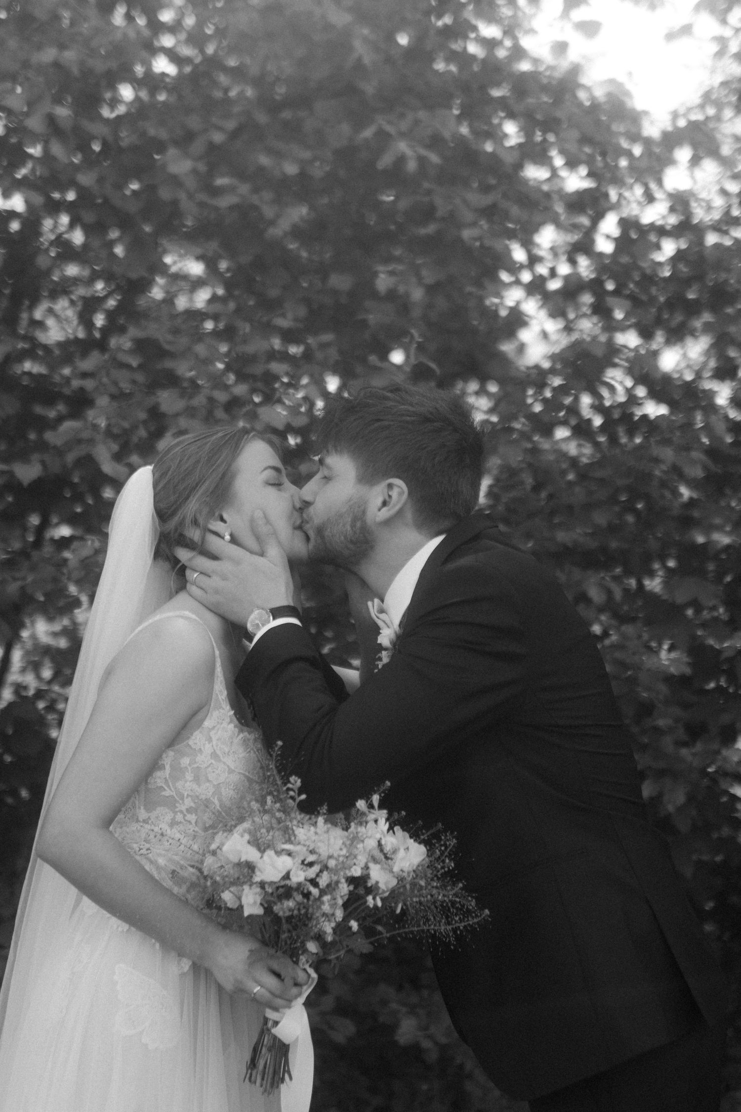 Intimate black and white photo of newlyweds kissing in a garden setting.