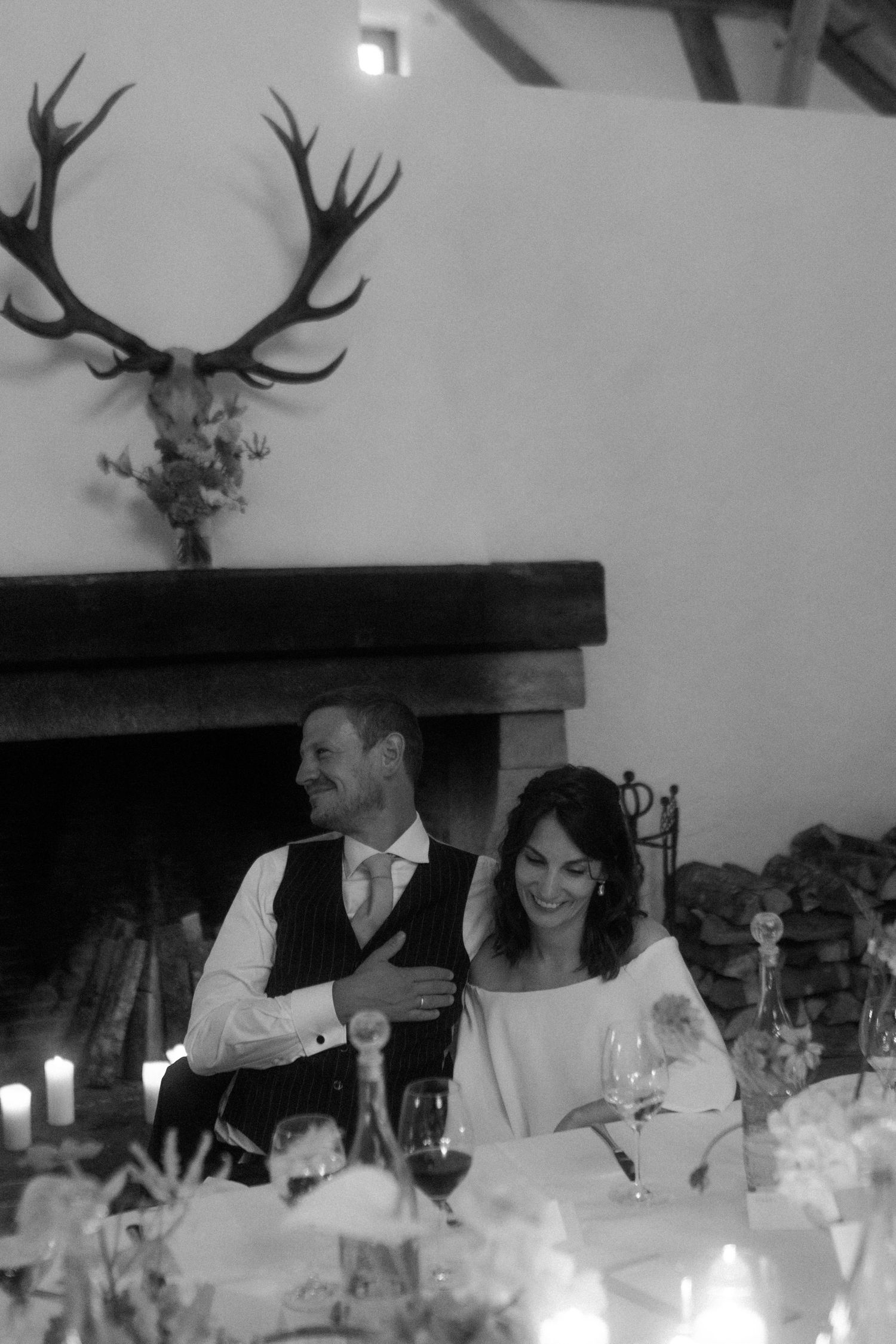 Black and white wedding reception photo with mounted antlers above fireplace.
