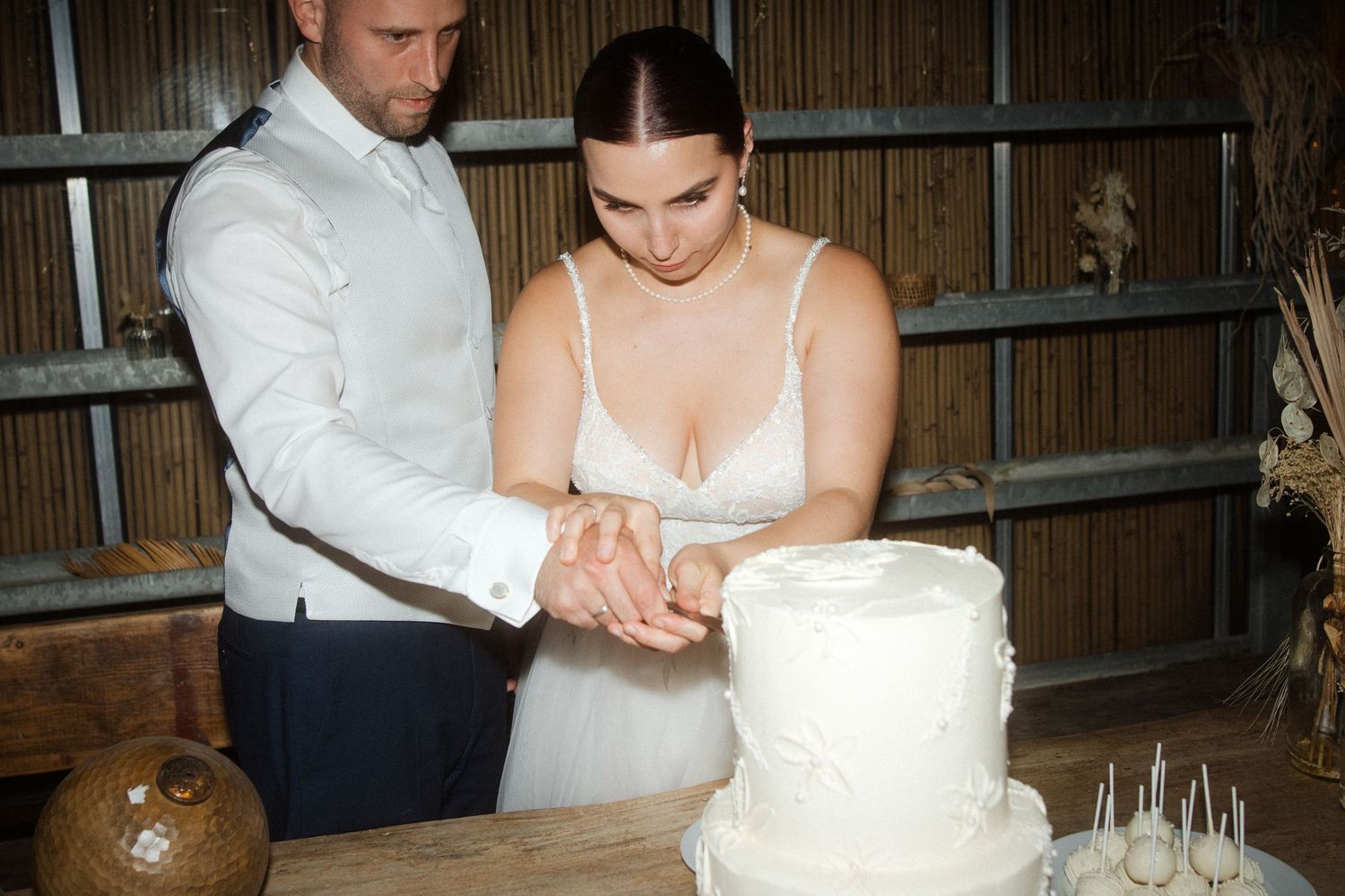Newlyweds jointly slice into their white tiered wedding cake during the reception.
