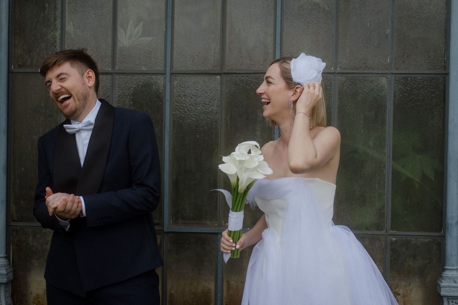 A candid moment captured against a glass conservatory wall with white calla lilies.