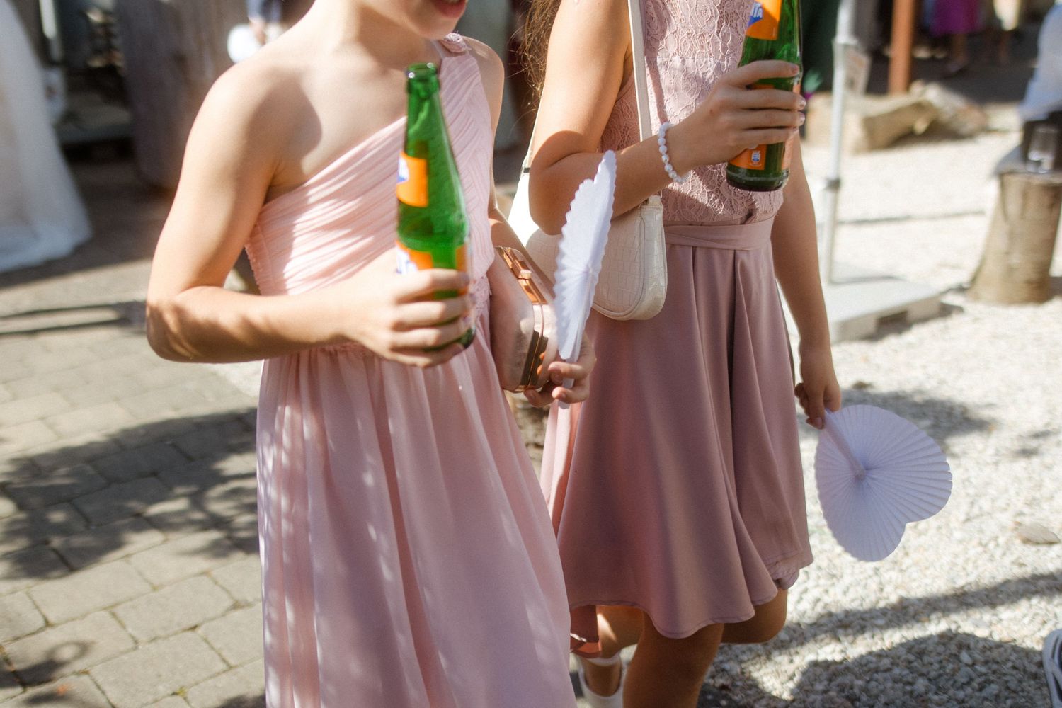 Bridesmaids in pink dresses holding drinks during outdoor wedding celebration.