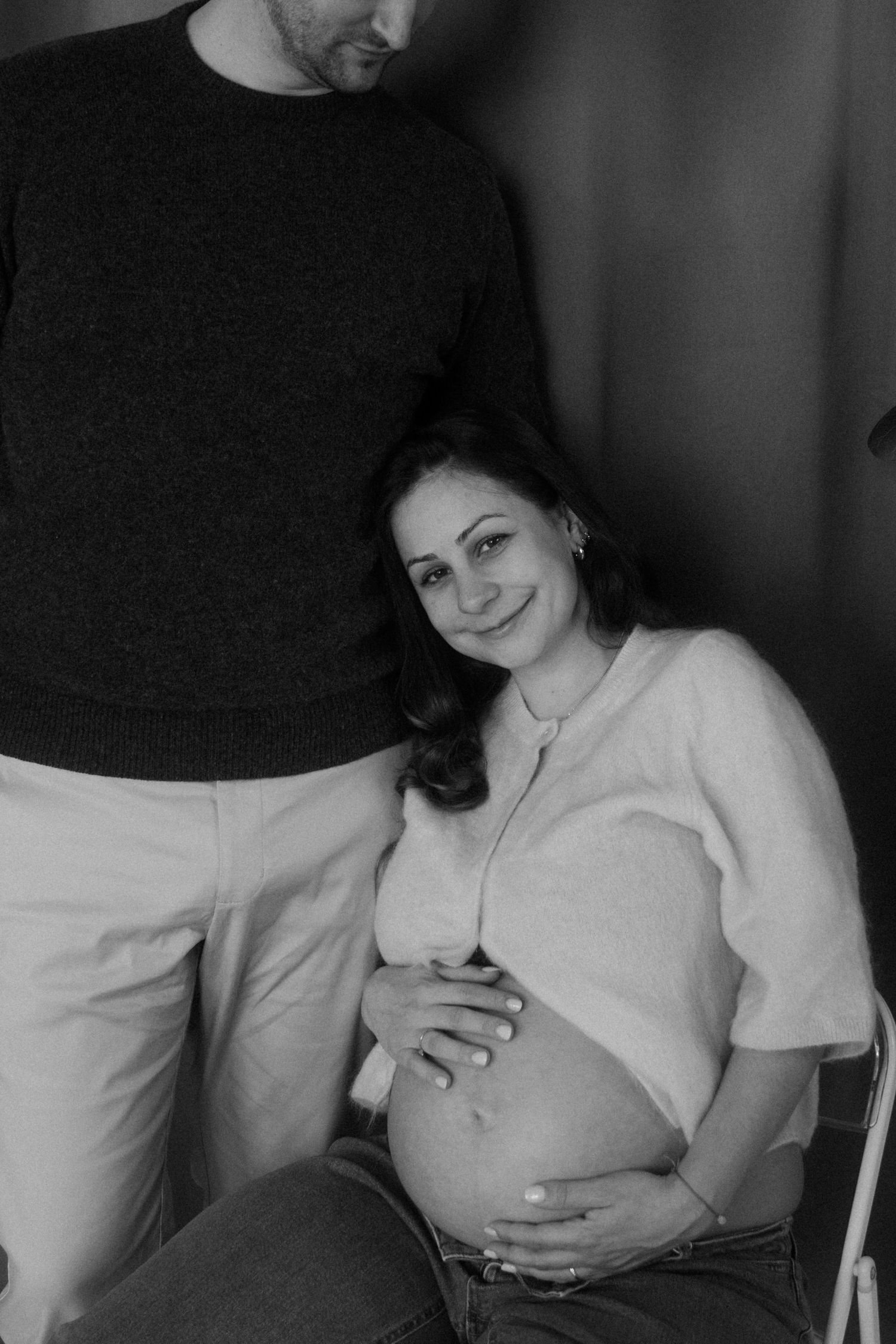 Black and white maternity photo showing a couple with the pregnant woman wearing a white shirt and touching her belly.