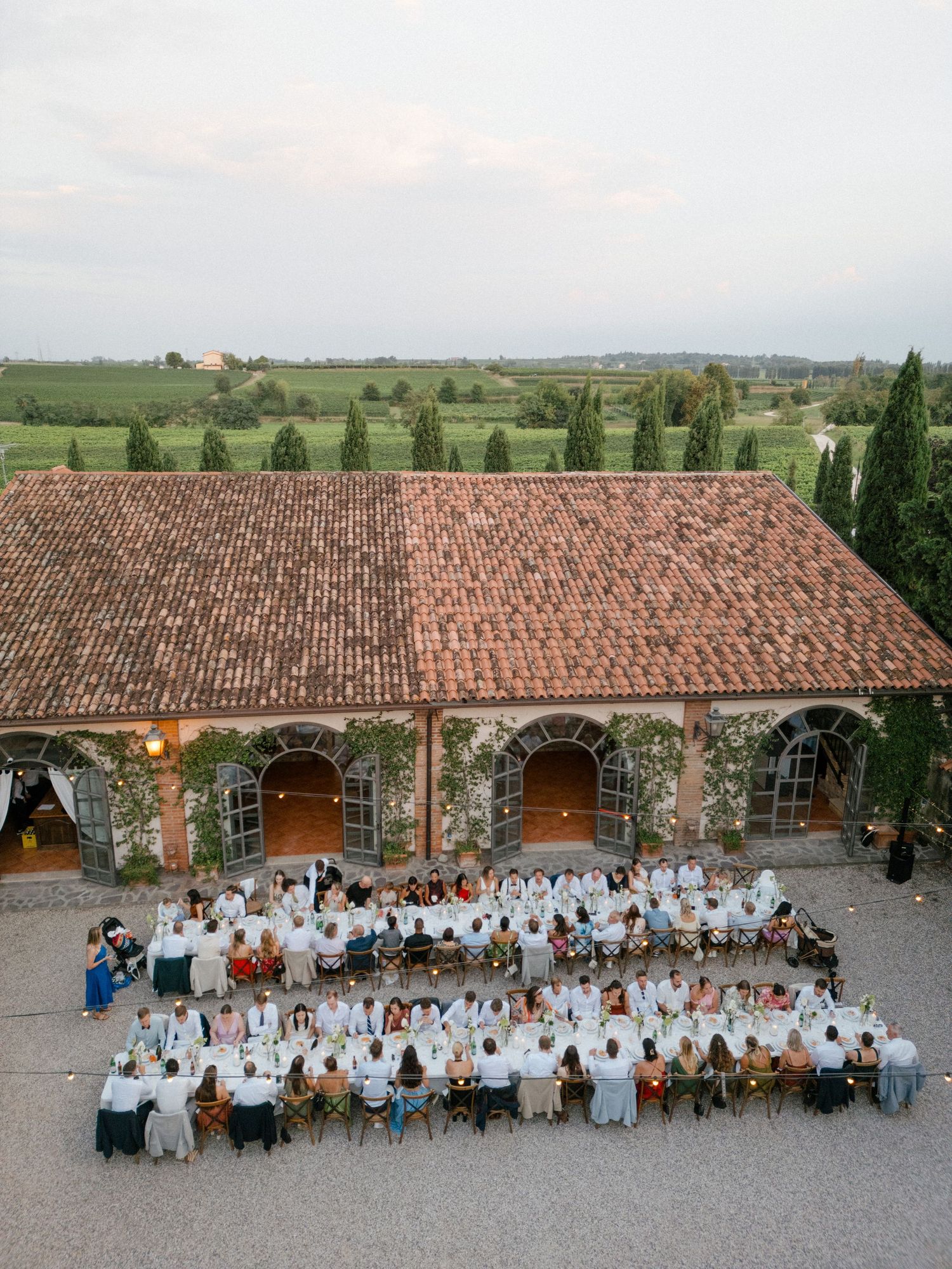 Large group photo of wedding guests gathered outside a rustic stone building with arched doorways.