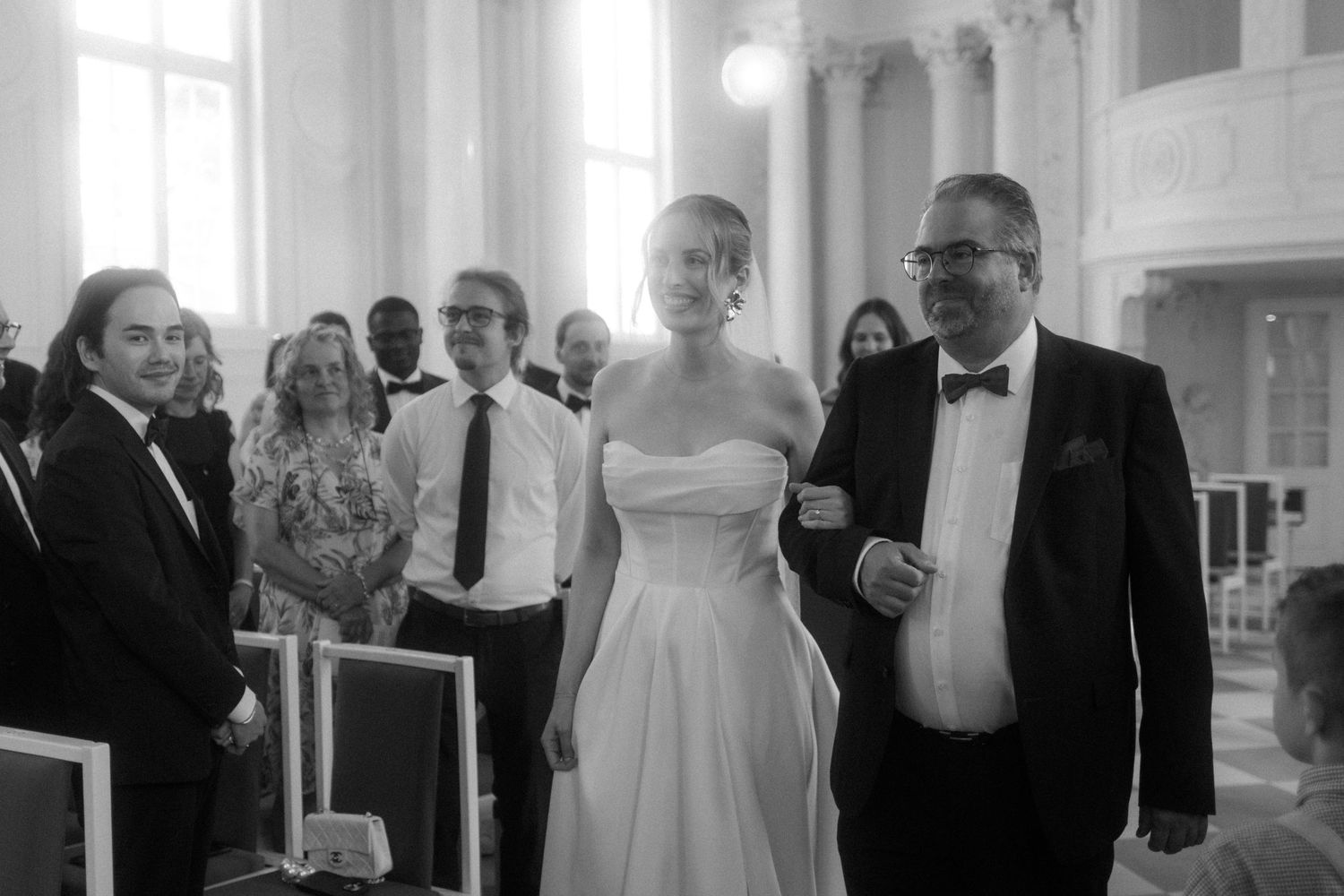 Elegant wedding ceremony in a grand white columned hall with guests looking on.