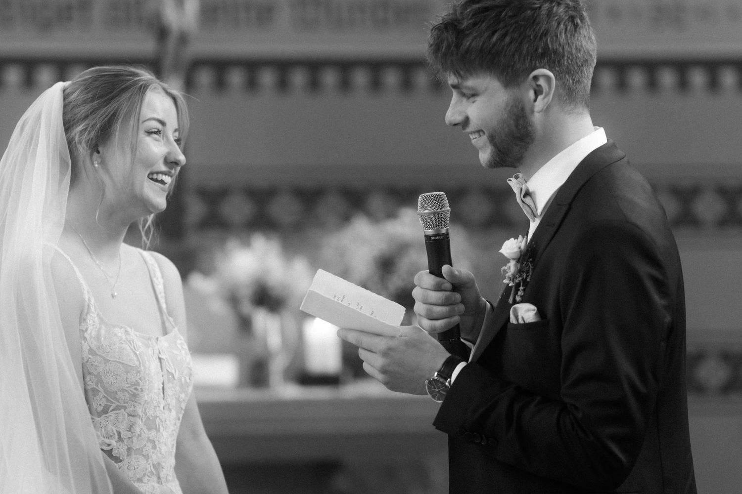 Bride and groom sharing joyful moment during wedding ceremony speeches with microphones.