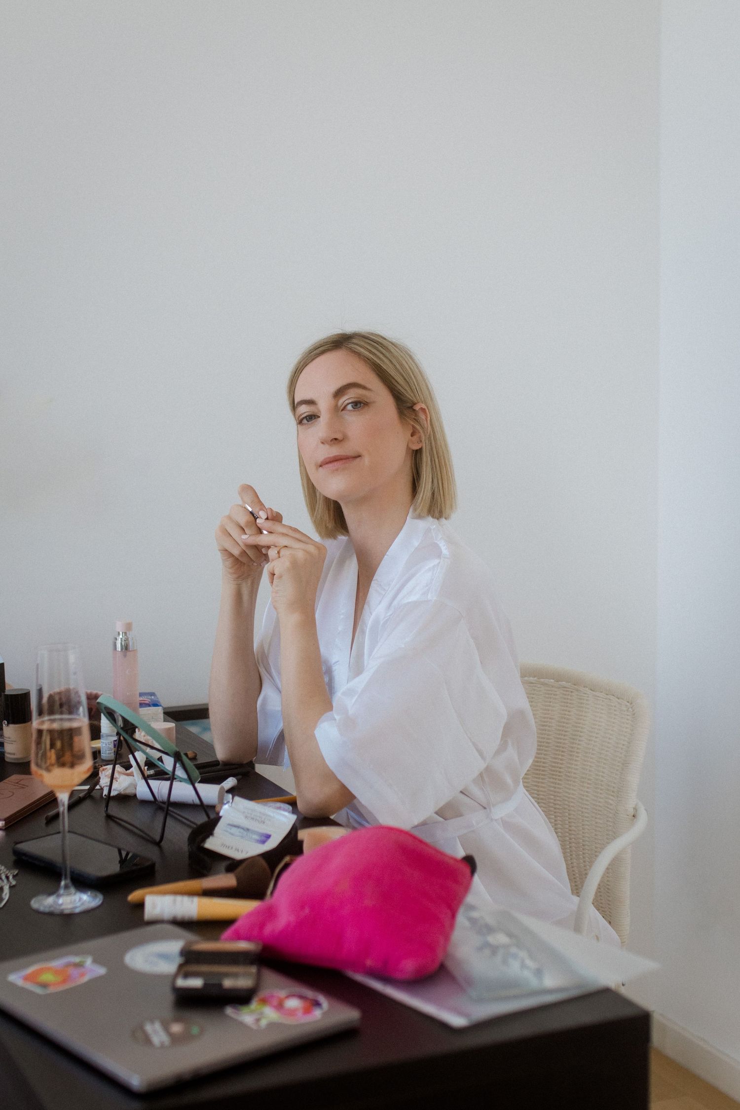 Person in white robe sitting at vanity table with makeup supplies.