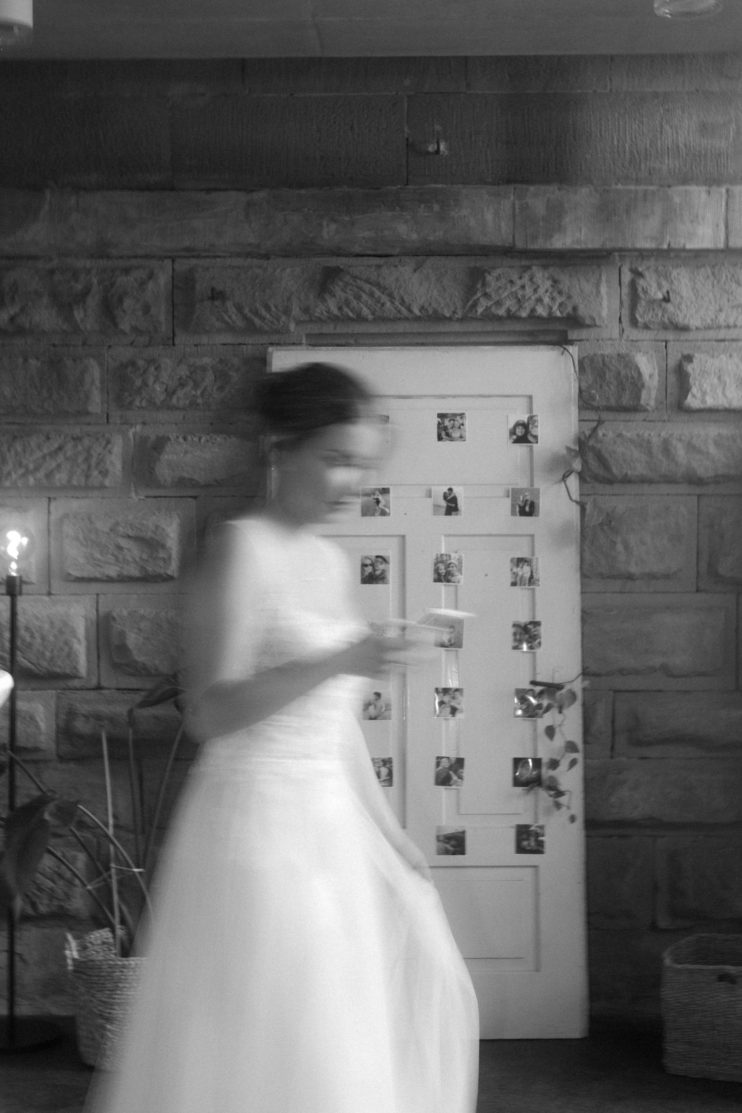 Motion blur of person in white dress looking at photo display on stone wall.