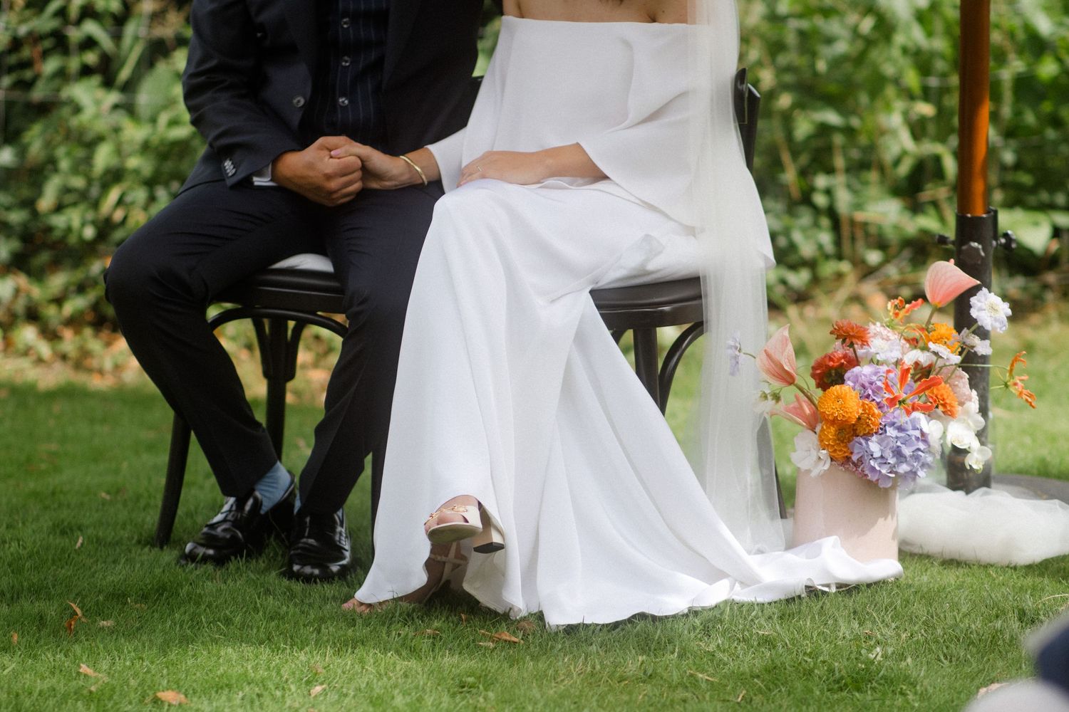 Detail shot of bride and groom sitting on chairs during outdoor wedding ceremony.