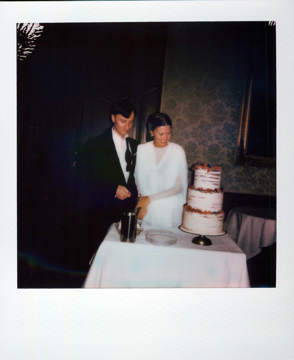 Two-tiered white frosted cake with decorative details being displayed on a table at an indoor event.
