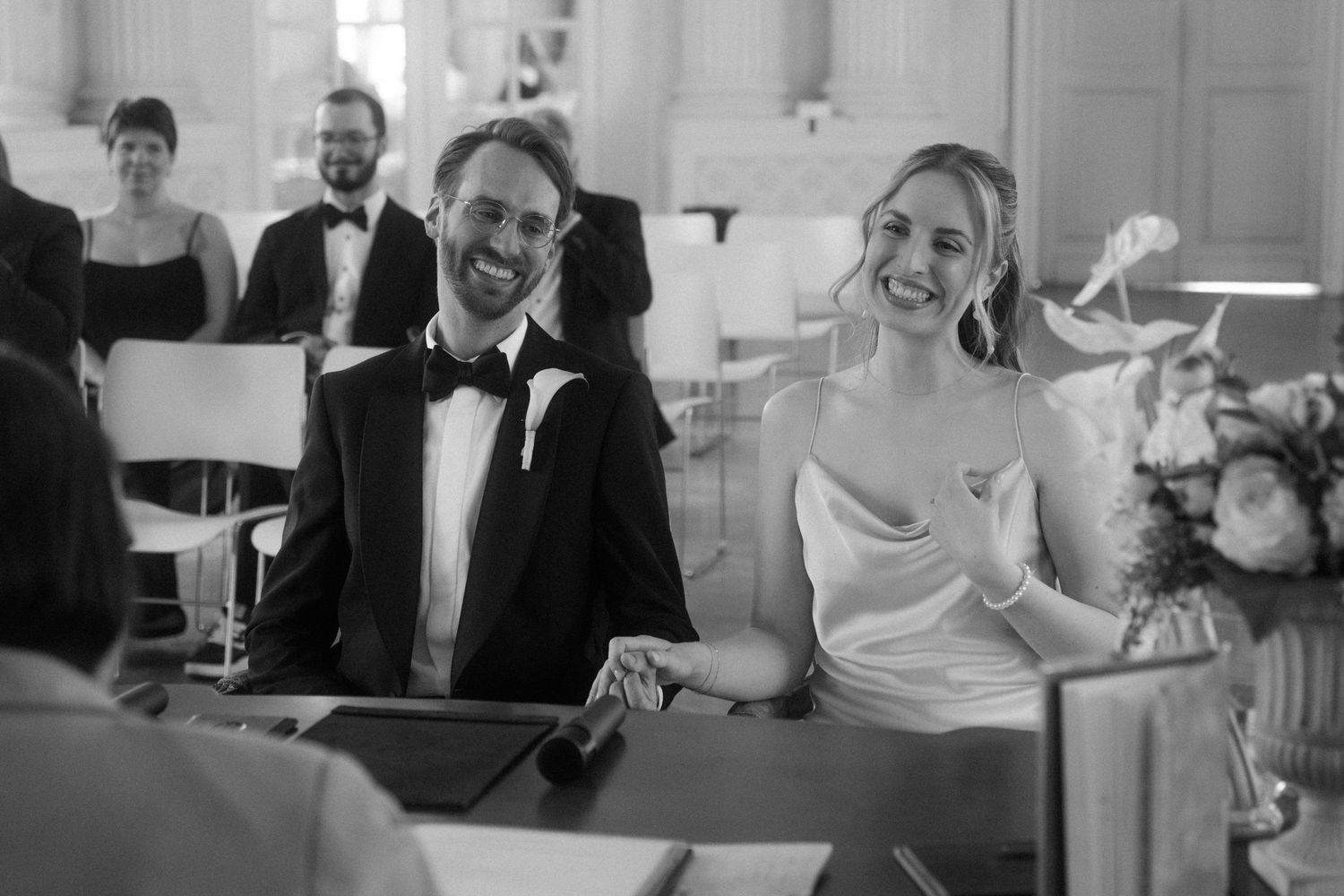 Wedding ceremony participants seated in an elegant white hall.