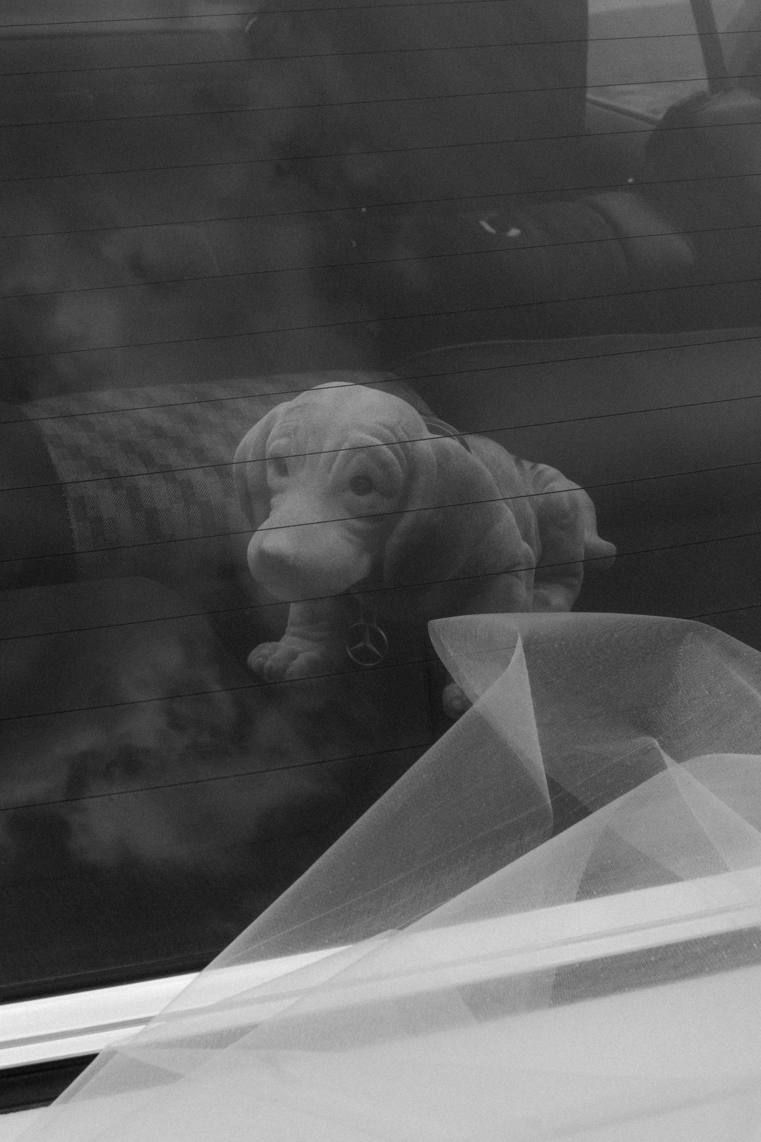 A wedding veil draped over a car window creating an artistic reflection.