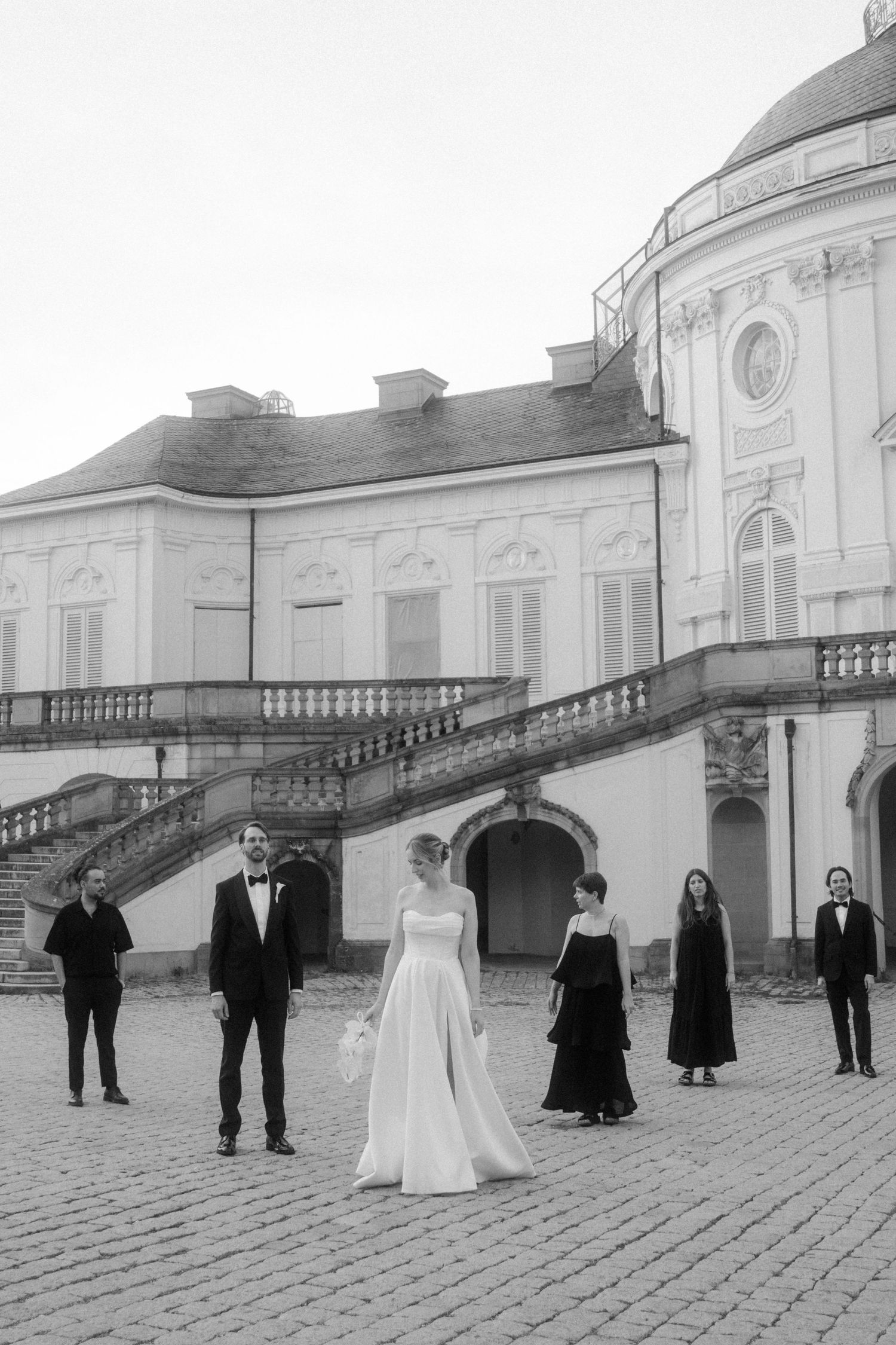 Wedding party arranged in front of a classical domed building with cobblestone courtyard.