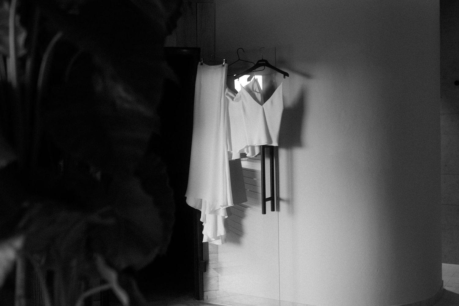 A white dress shirt and vest hanging in dim lighting against a wall.