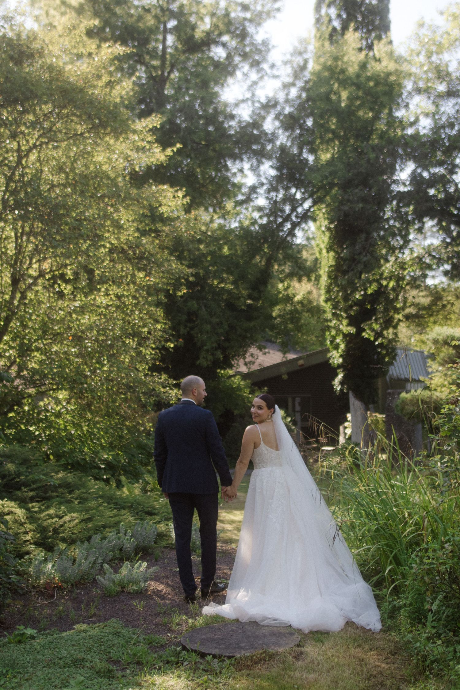 Couple walks hand in hand through a verdant garden path on their wedding day.