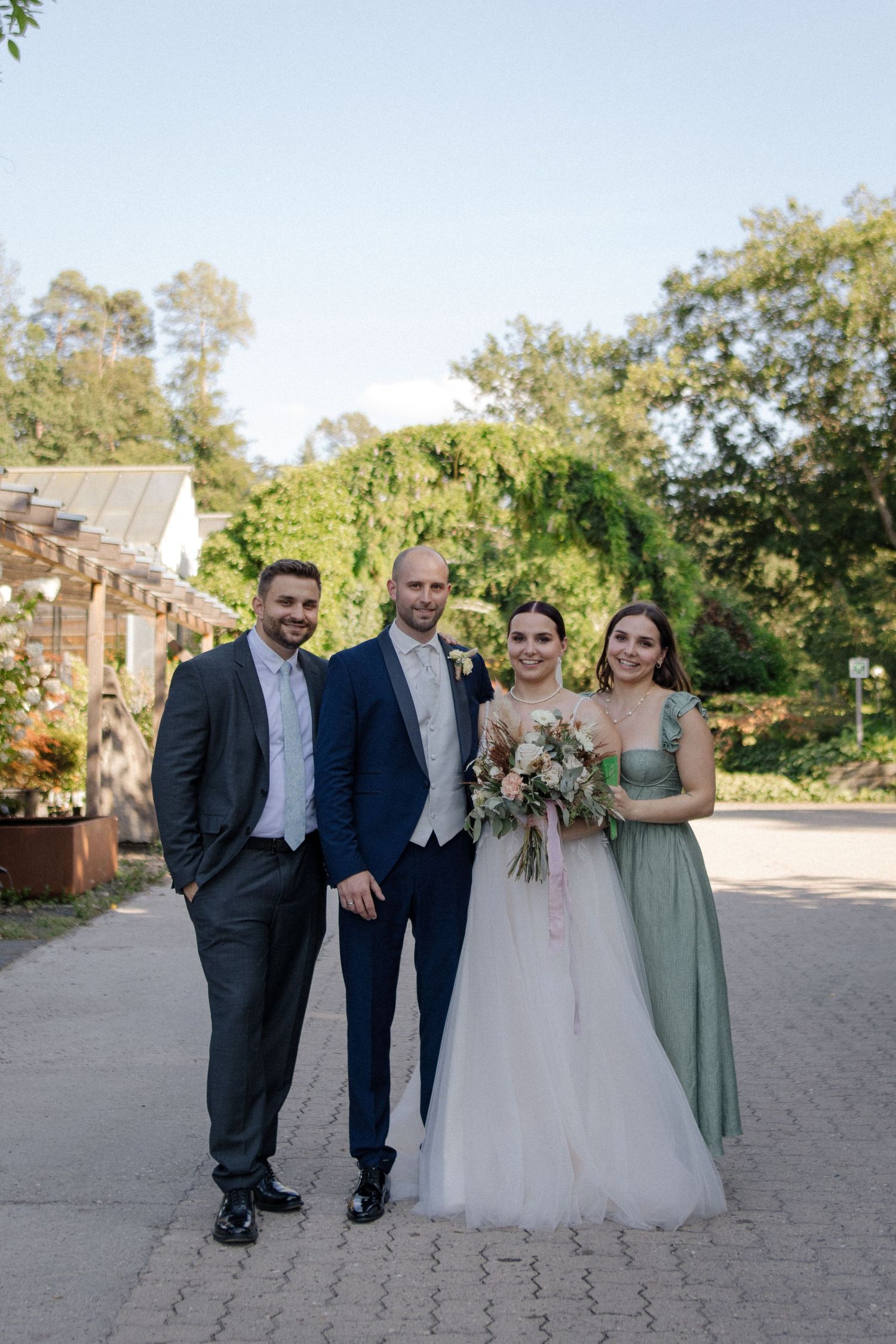 A wedding party of four people posing outdoors in formal attire with the bride in a white gown.