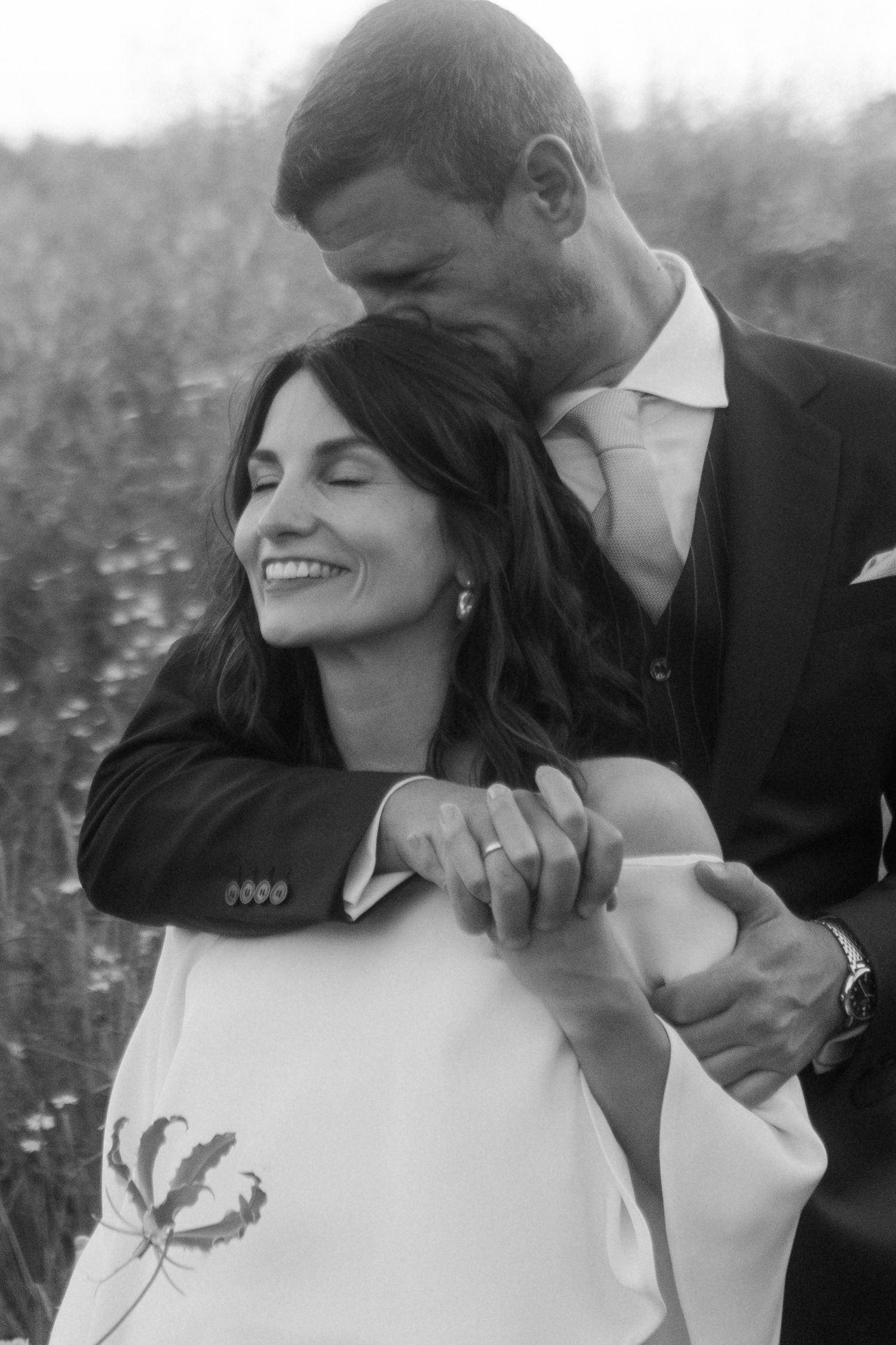 A romantic black and white portrait of a couple embracing in a wildflower field.