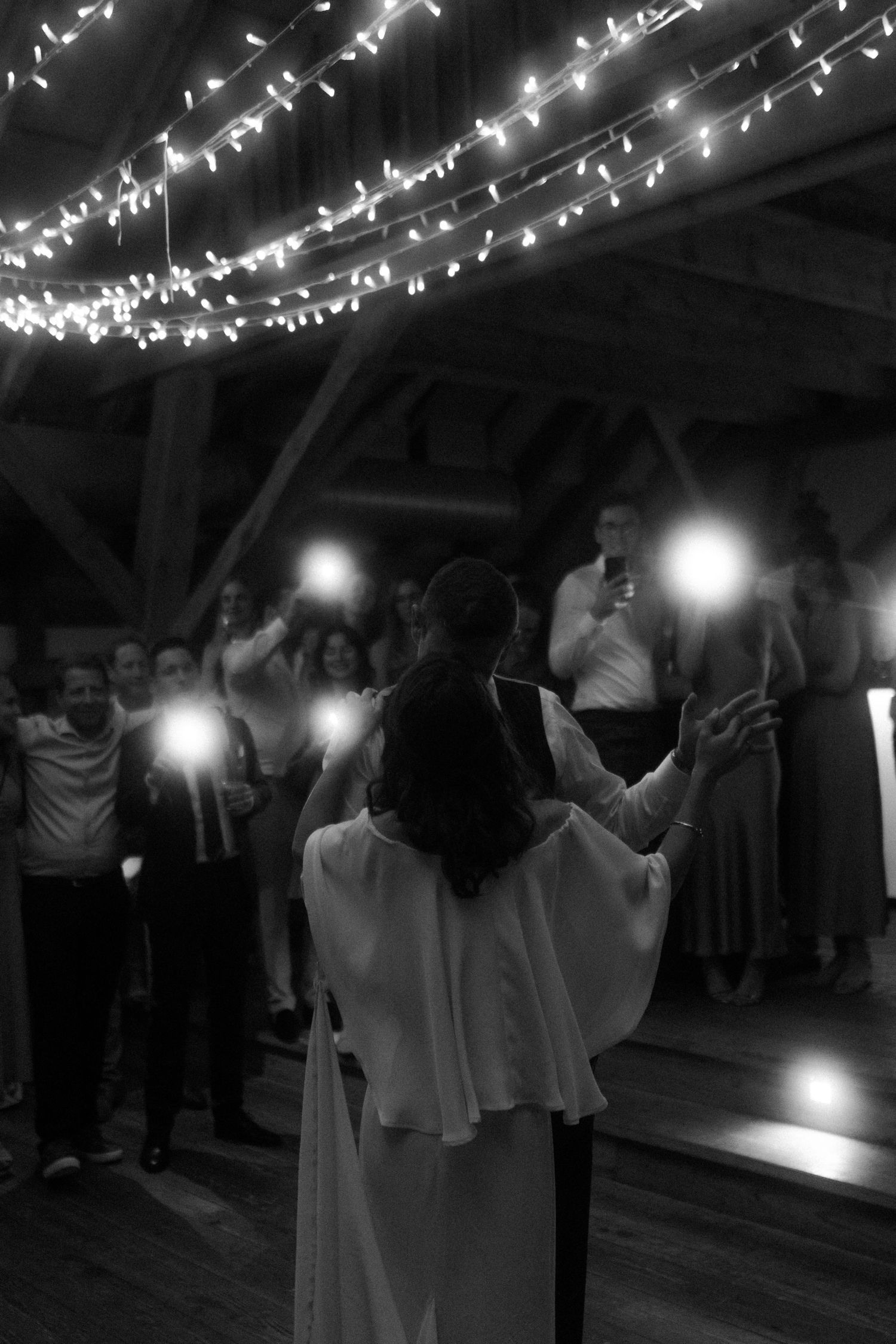 Couple dancing under string lights at a romantic wedding reception in black and white.