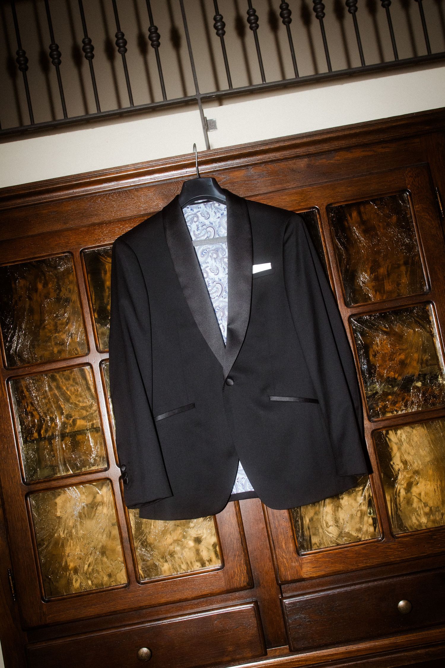 Black formal suit jacket hanging on display against wooden vintage cabinets.