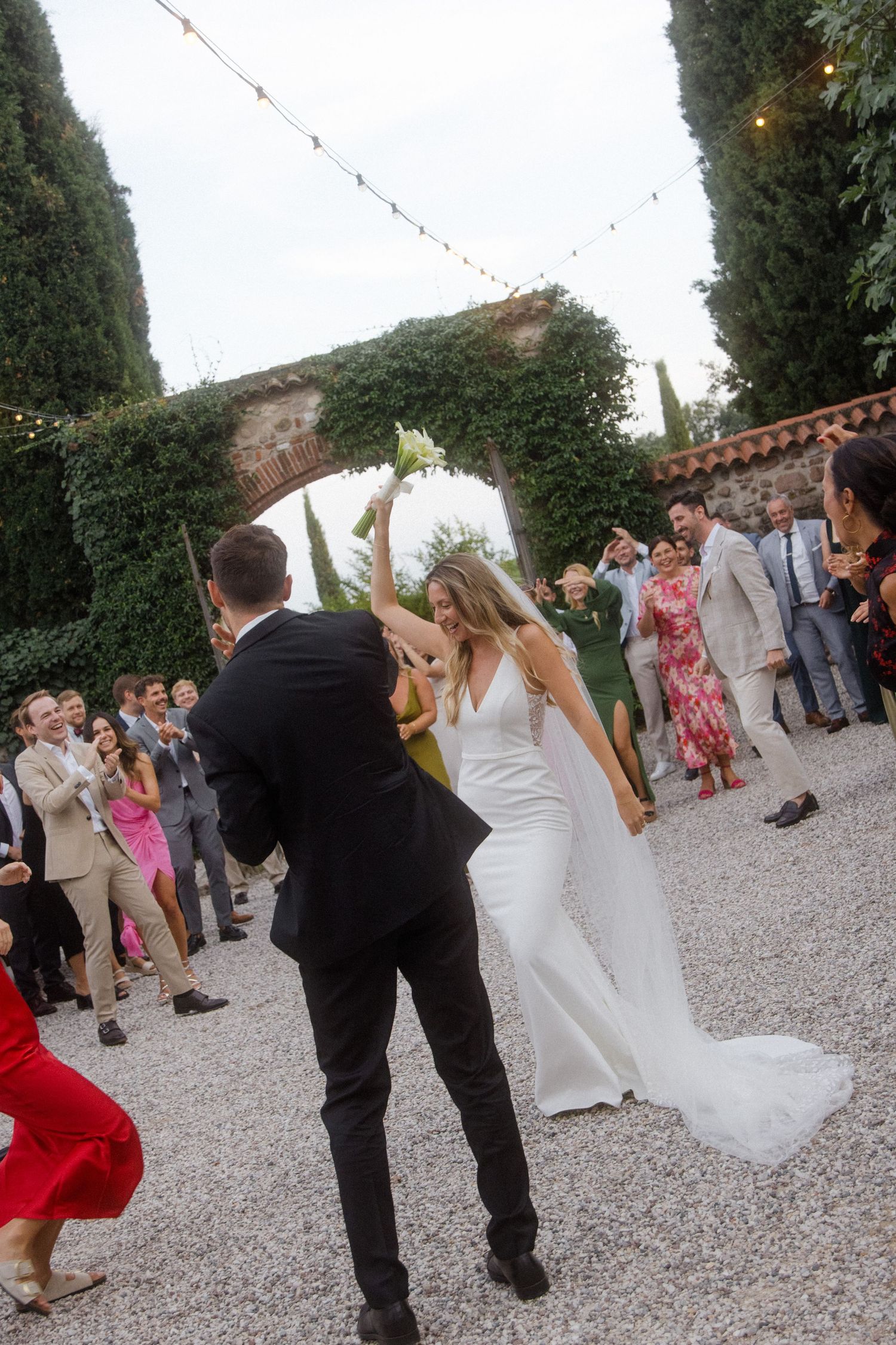 Wedding guests perform group dance moves at outdoor reception with string lights.
