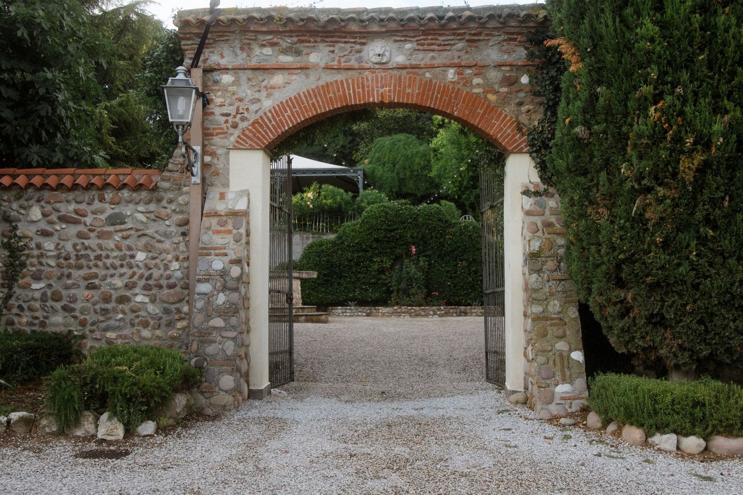 Stone entrance gate with brick arch and gravel path leading to garden.