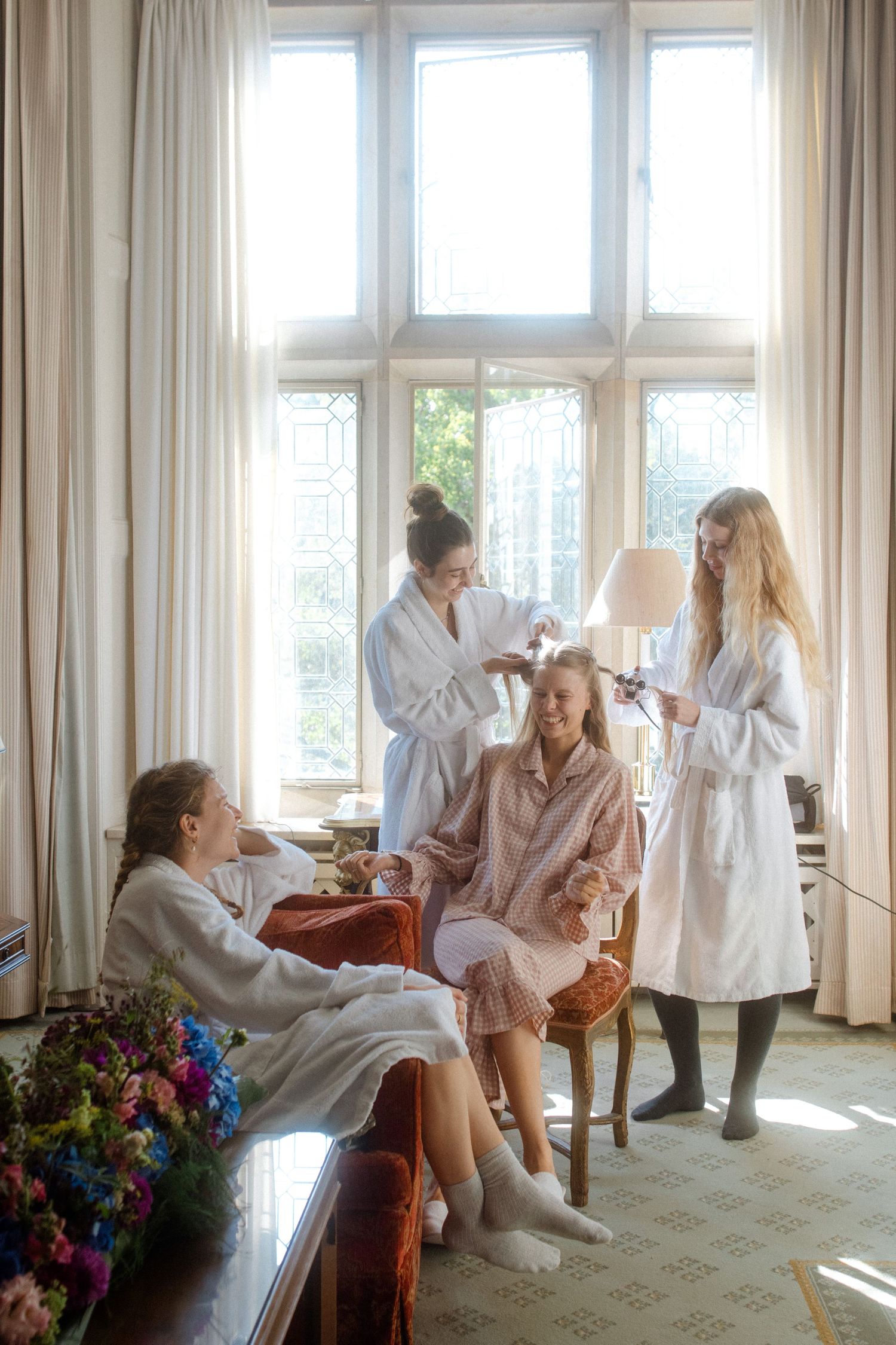 Group relaxing in white robes by sunny windows with colorful flowers.