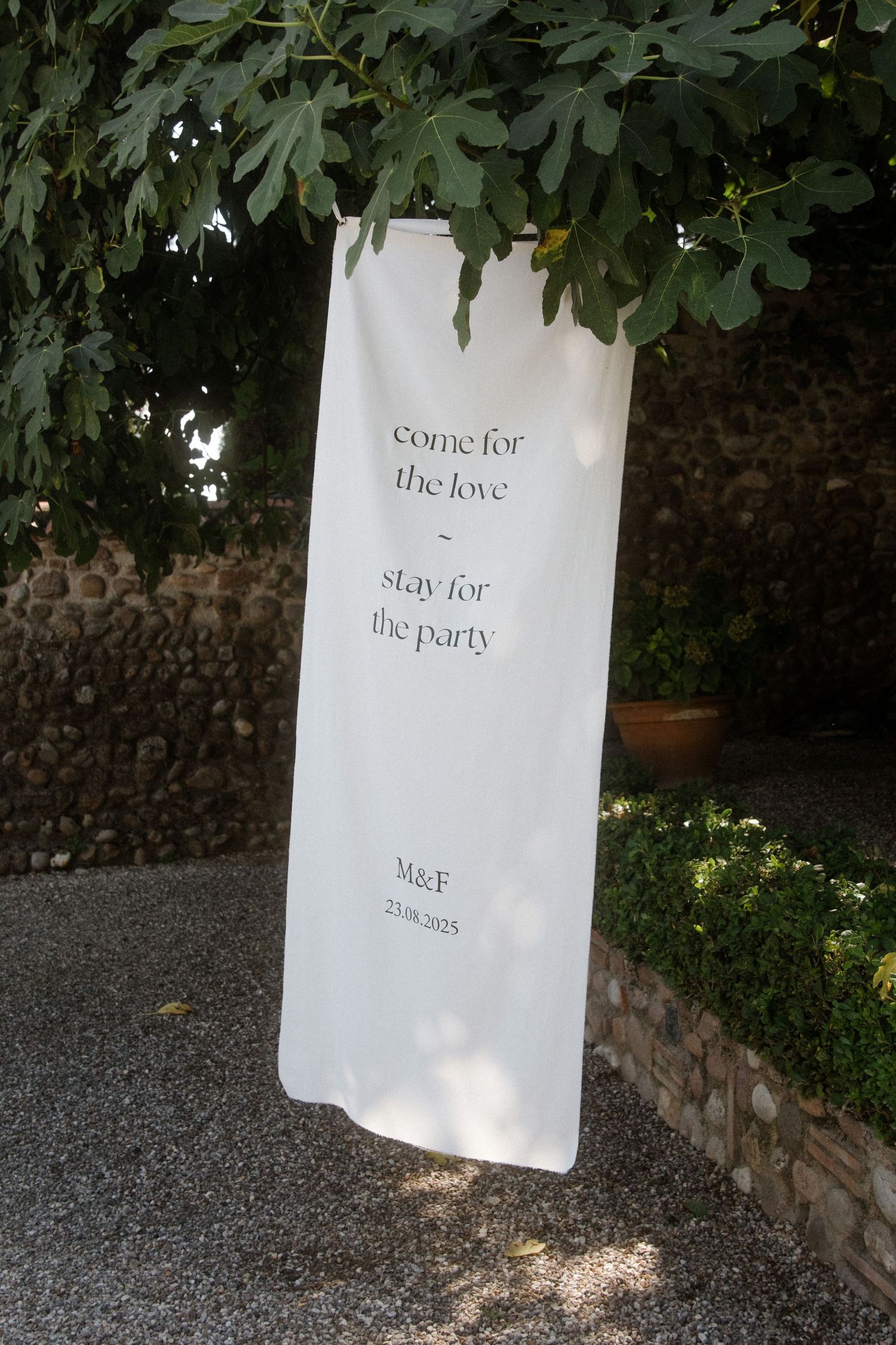 White banner with text 'come for the love stay for the party' hanging under green foliage.