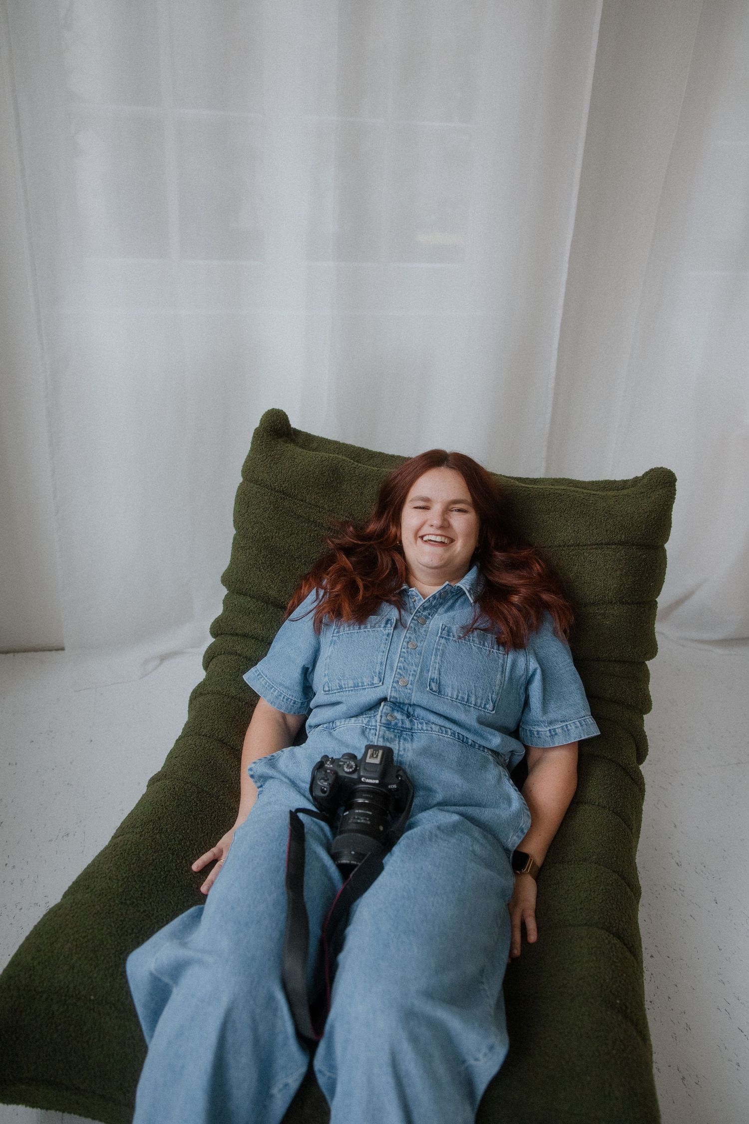 Person in denim outfit lying on an olive green cushion with a camera, shown in multiple relaxed poses.
