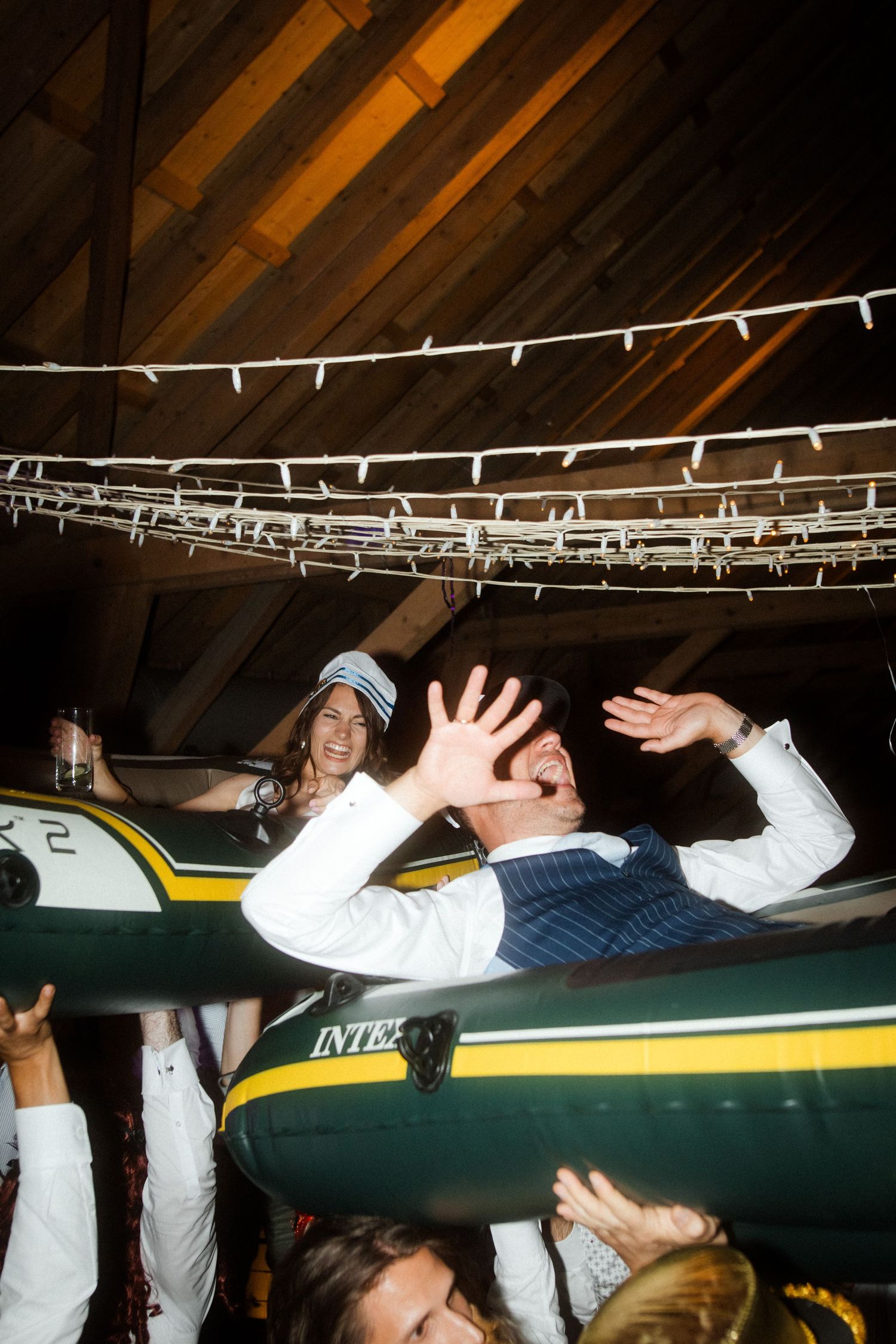 People lifting an inflatable boat overhead during an indoor celebration event.