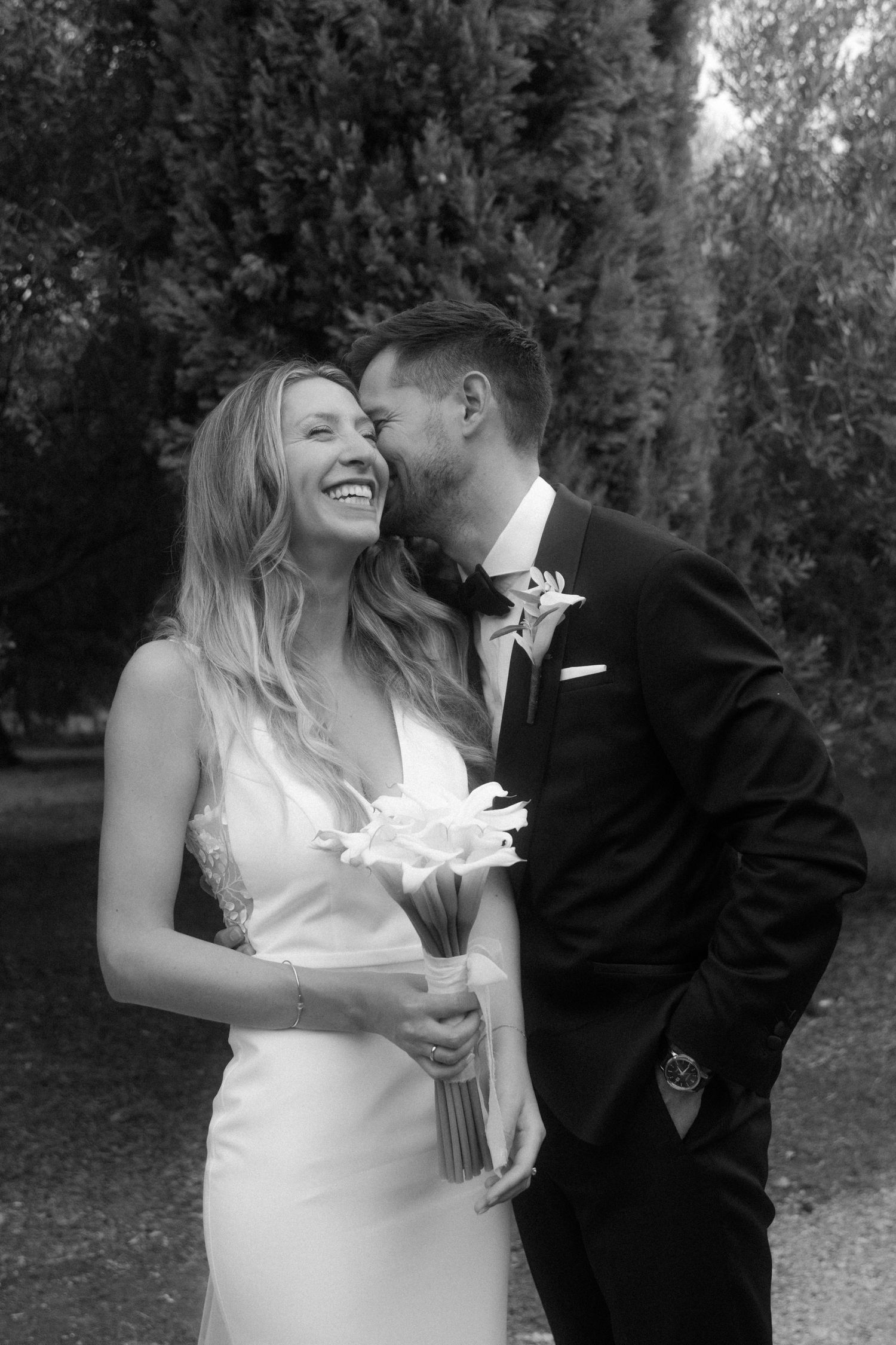 A joyful moment between newlyweds sharing laughter in a garden setting.