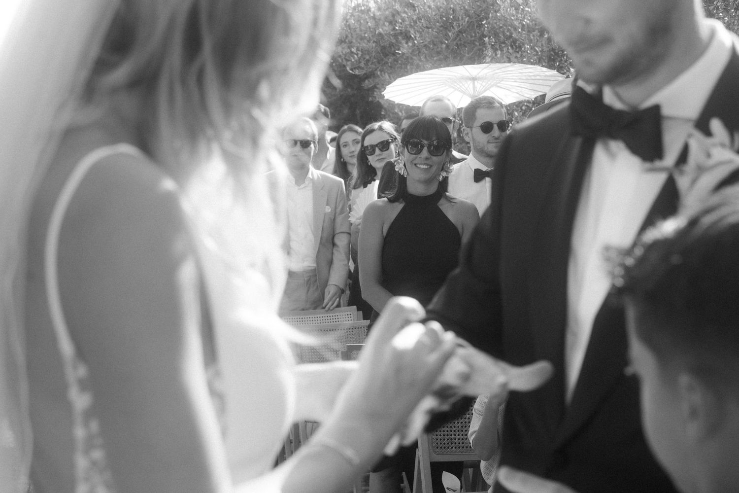 Black and white capture of wedding ceremony ring exchange with guests looking on.